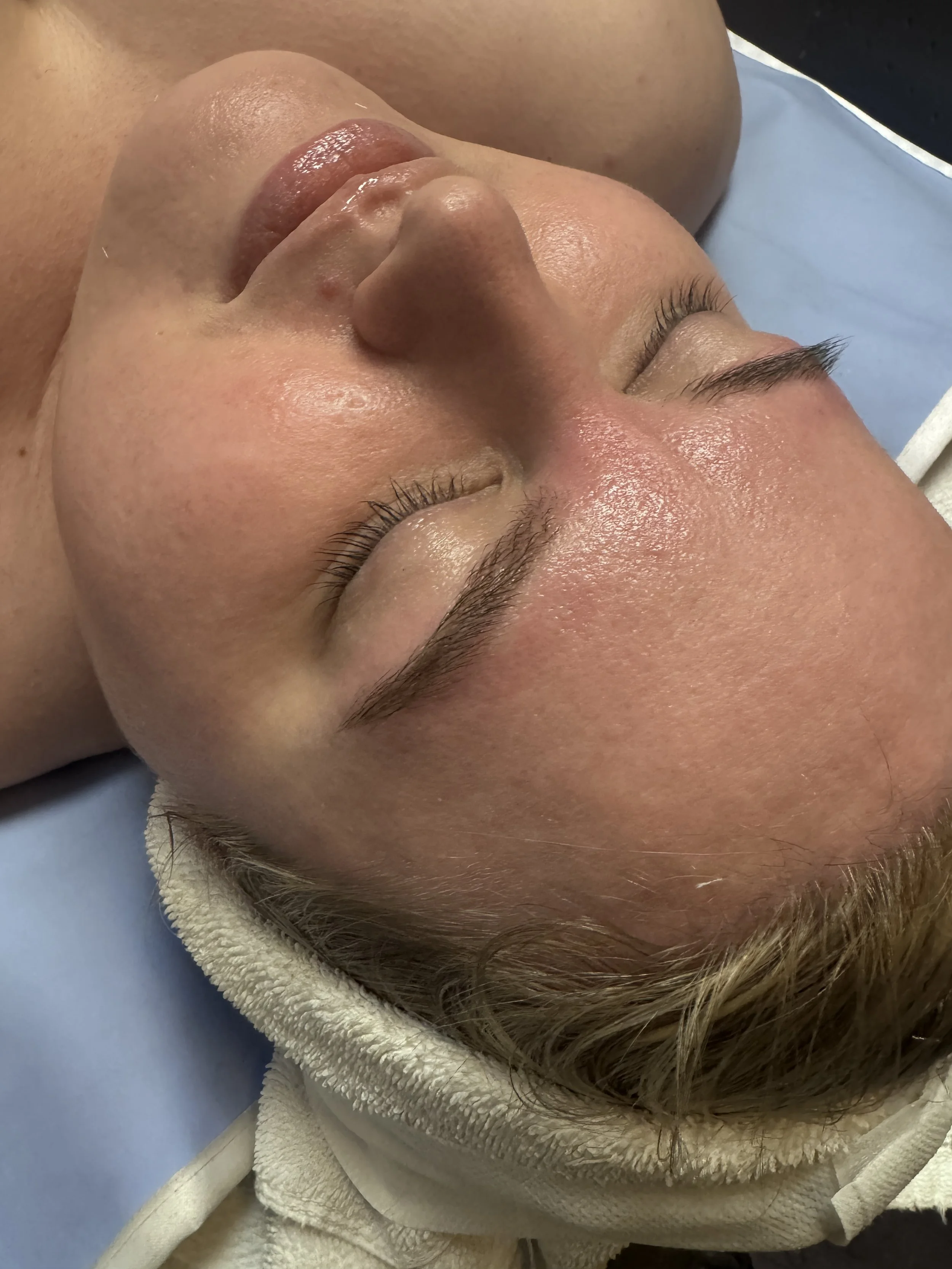 Close-up of a woman lying down with her eyes closed, covered with a blanket, showing her nose, lips, and closed eyes with long eyelashes.