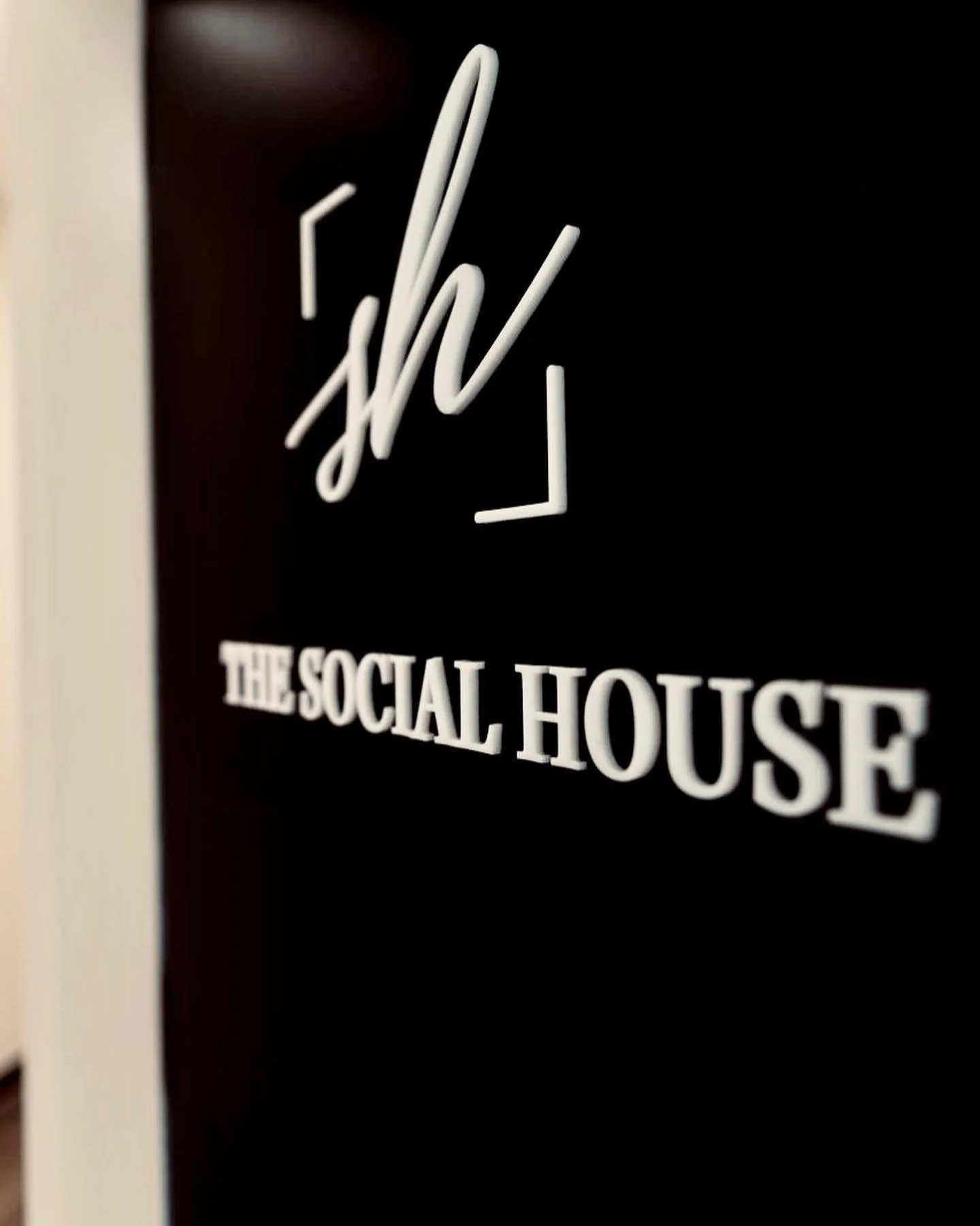 Close-up of a black sign with white text reading 'The Social House' and a stylized 'SH' logo above.