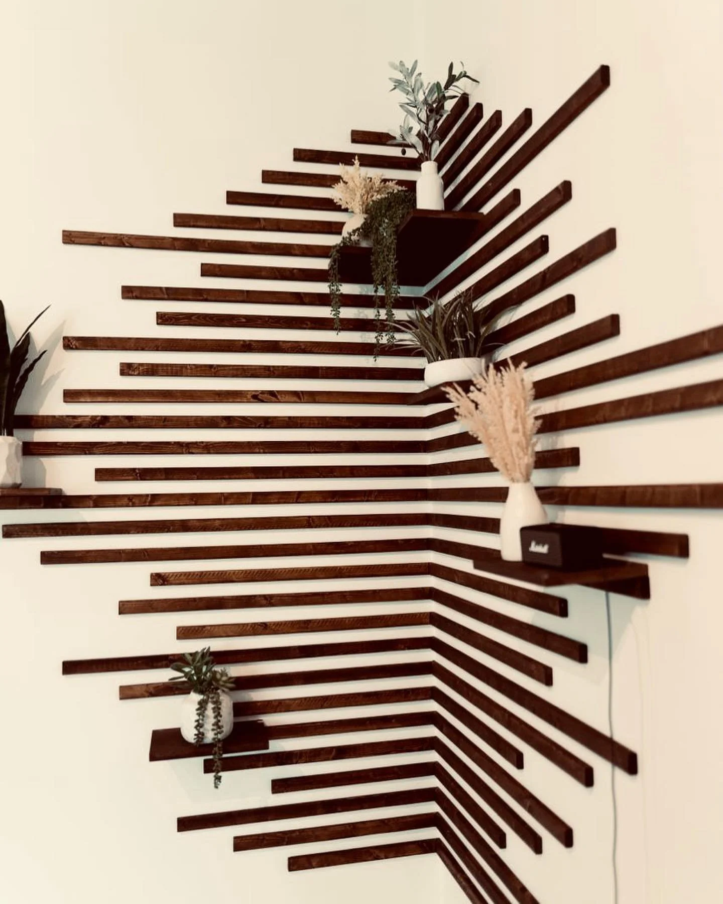 Decorative wall with dark wooden slats arranged in a geometric pattern, displaying white vases with greenery and dried flowers.