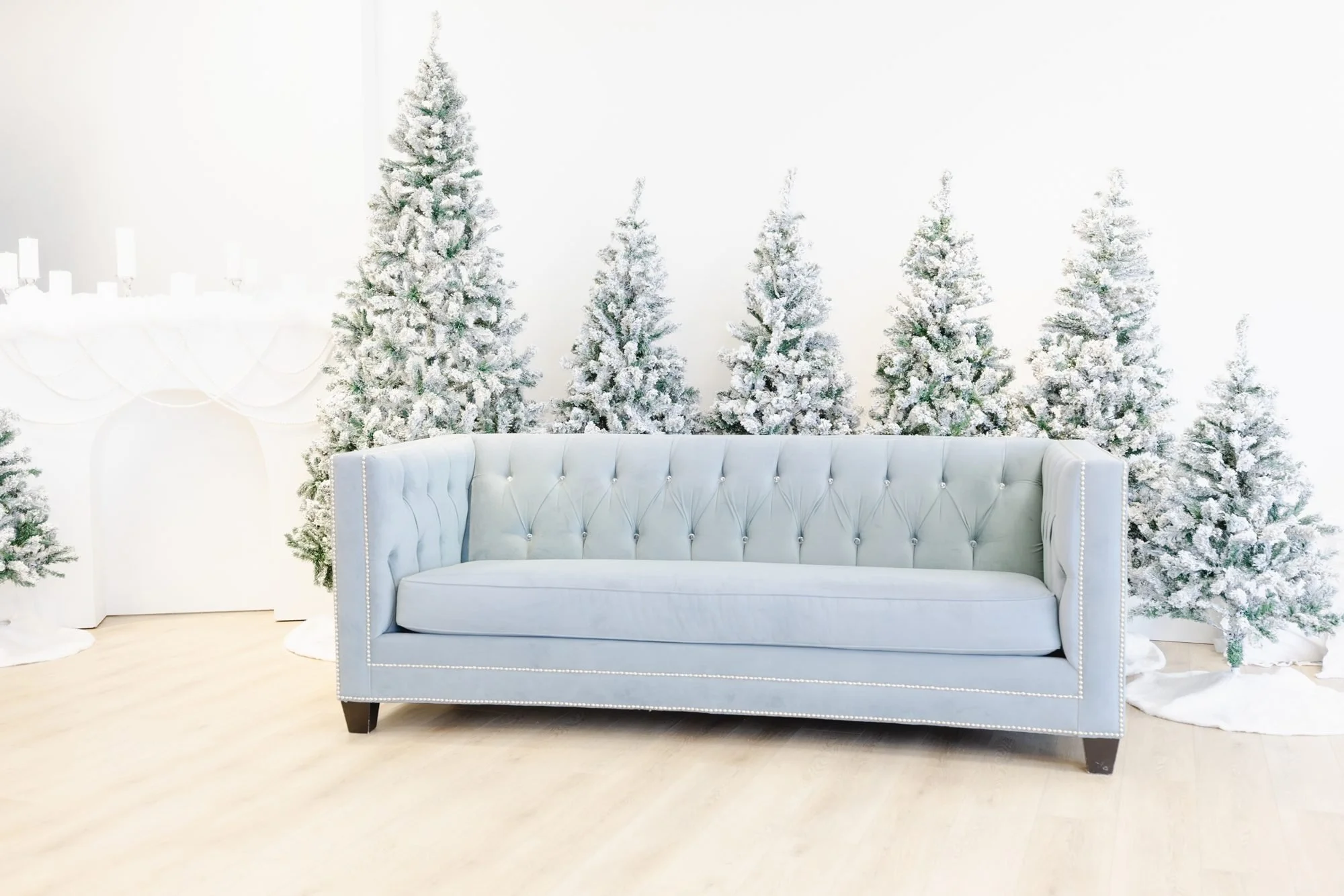 White tufted sofa in front of a backdrop of snow-covered artificial Christmas trees and white candles.