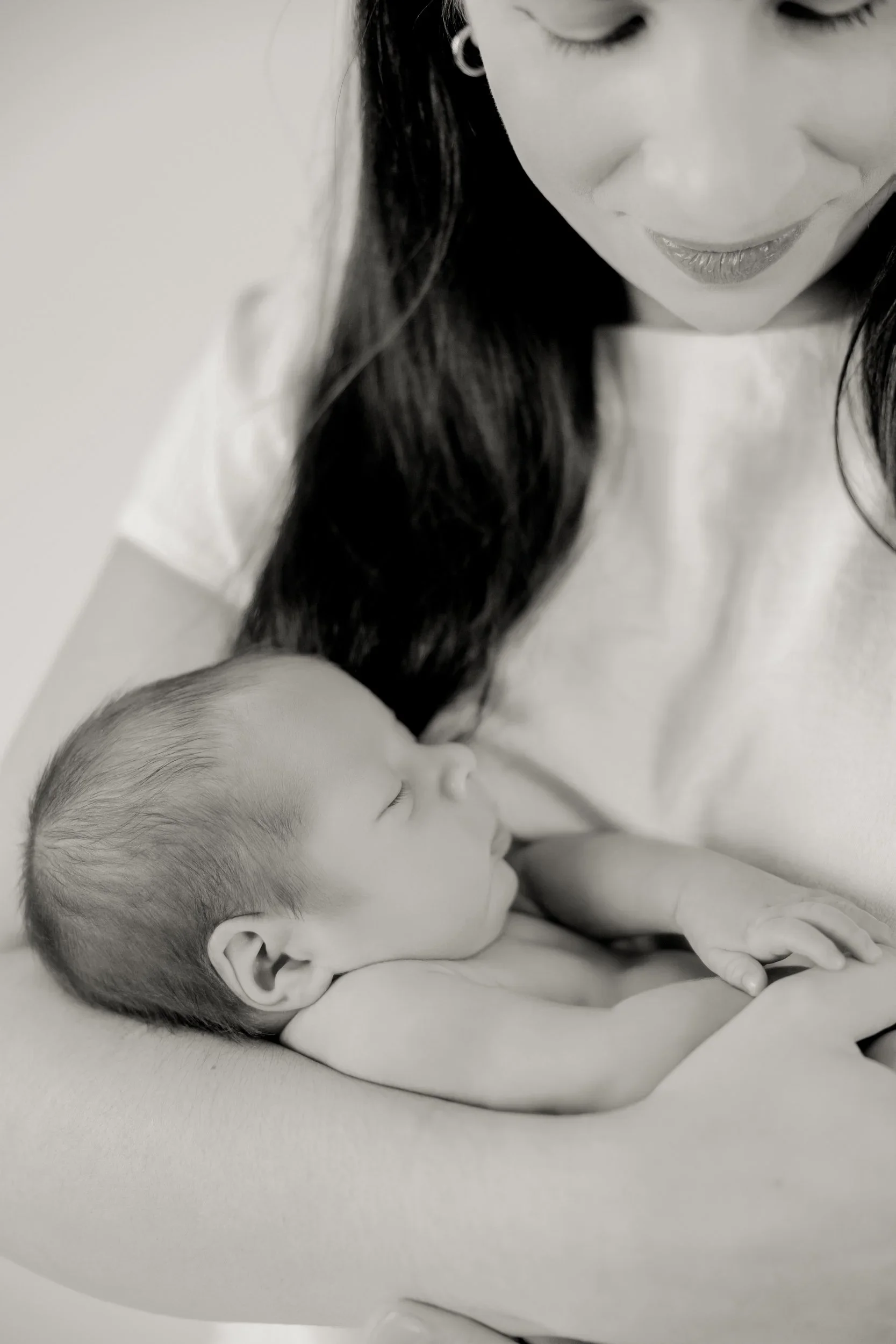Black and white photograph of a woman and a sleeping baby, both resting against each other, with the woman smiling gently.