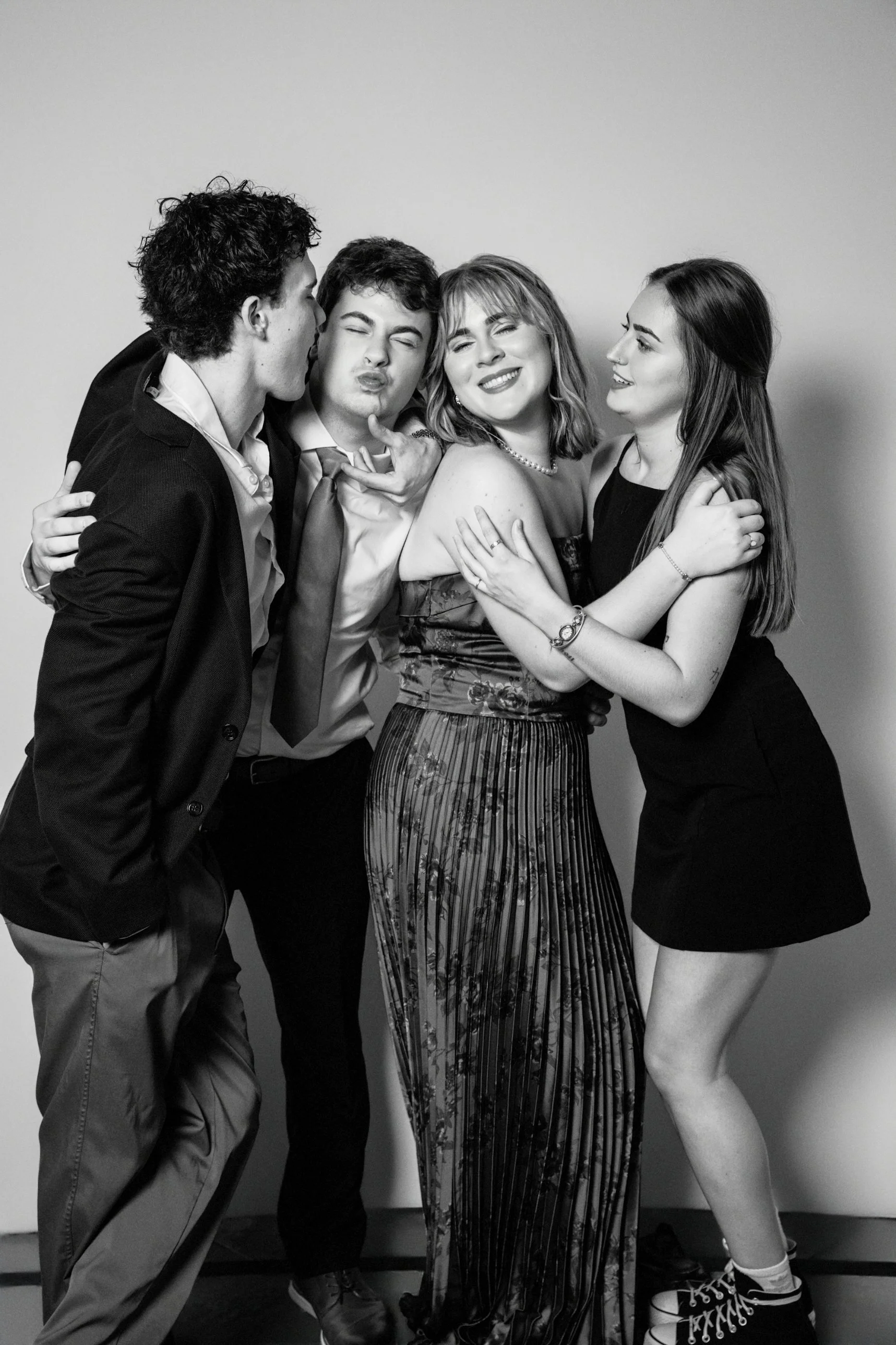 Black and white photo of five young adults closely grouped together, smiling and making playful faces, against a plain background.