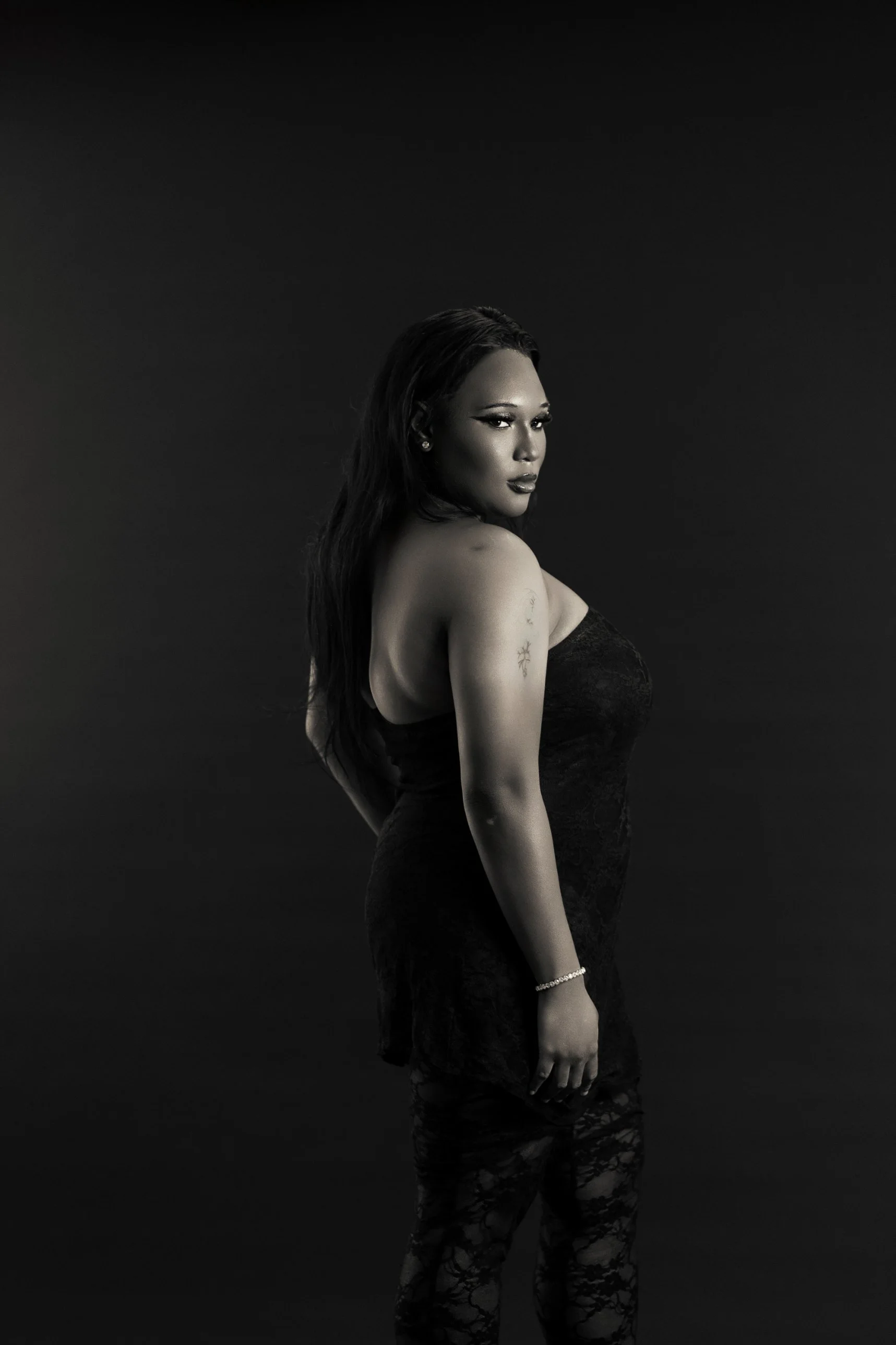 Black and white studio portrait at The Social House in Myrtle Beach: a woman in a black lace dress looking back over her shoulder against a dark backdrop.