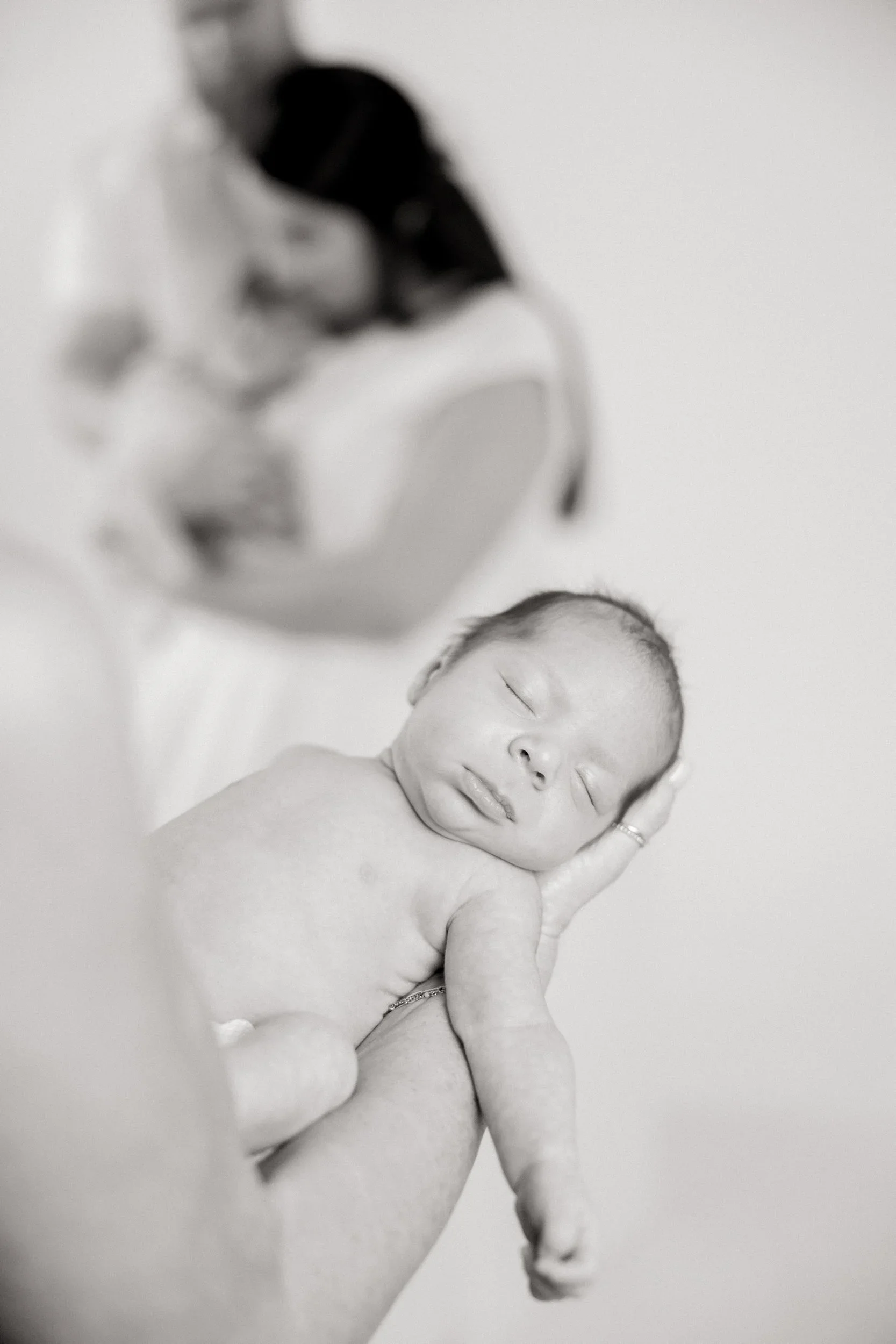 A newborn baby sleeping on a soft surface, with eyes closed and hand resting on its cheek.