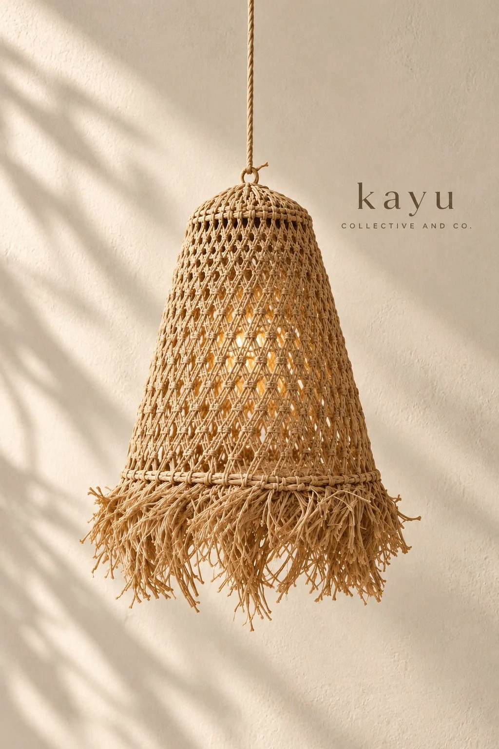 A woven rattan pendant lamp hanging from a ceiling with soft shadow patterns on the wall, branded with the text 'kayu COLLECTIVE AND CO.'.