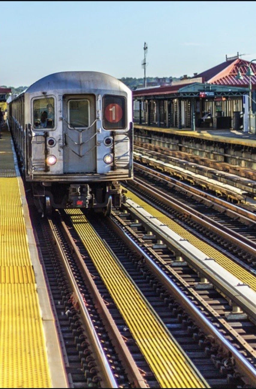 Subway train arriving at a station platform with yellow tactile paving and tracks in an urban setting.