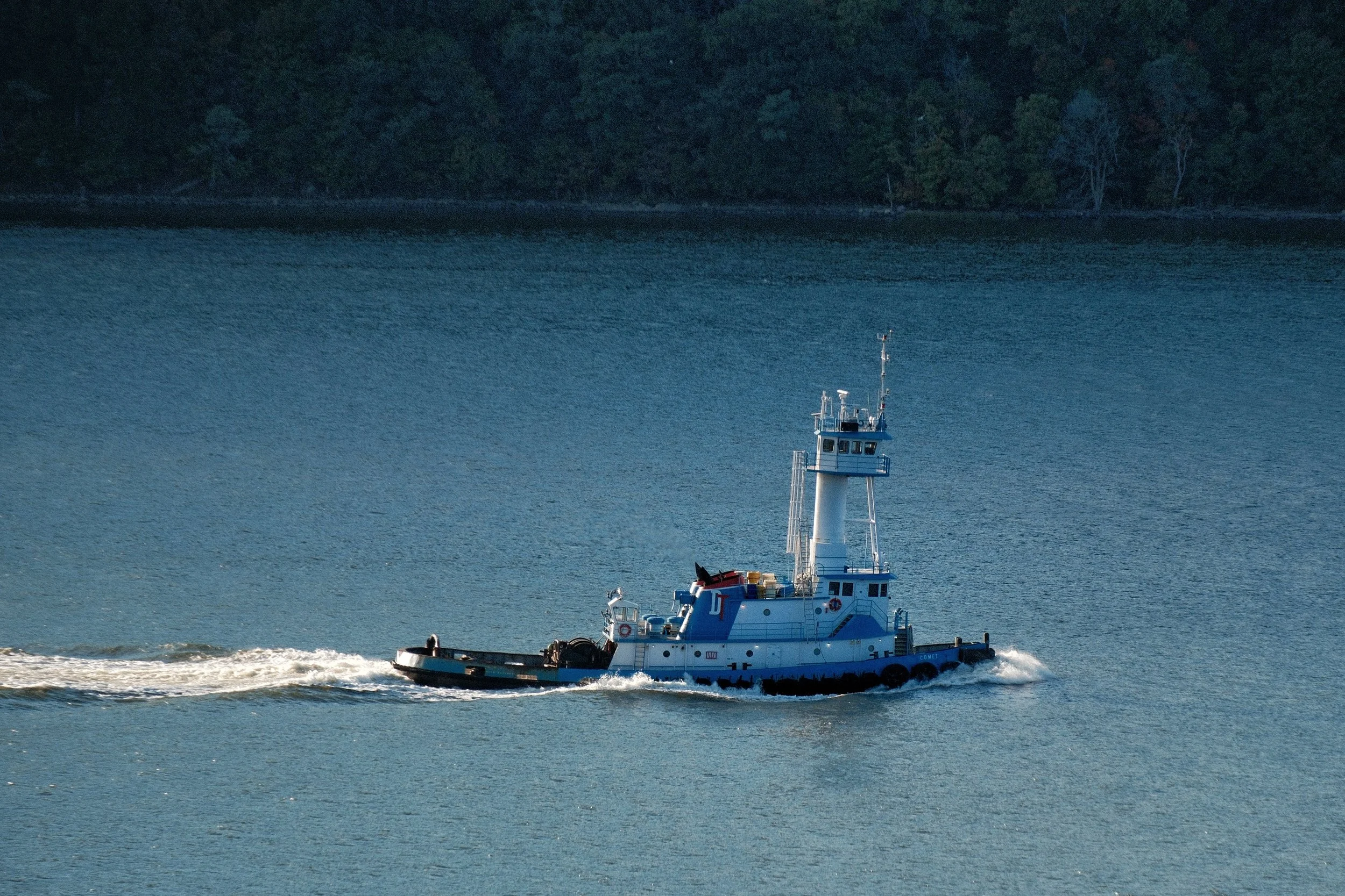 A tugboat named 'Comet' moving through the water, with a forested shoreline in the background.