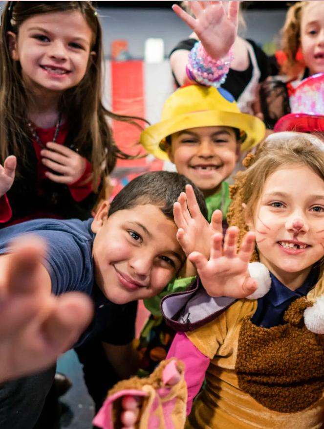 Smiling children in colorful costumes waving at the camera