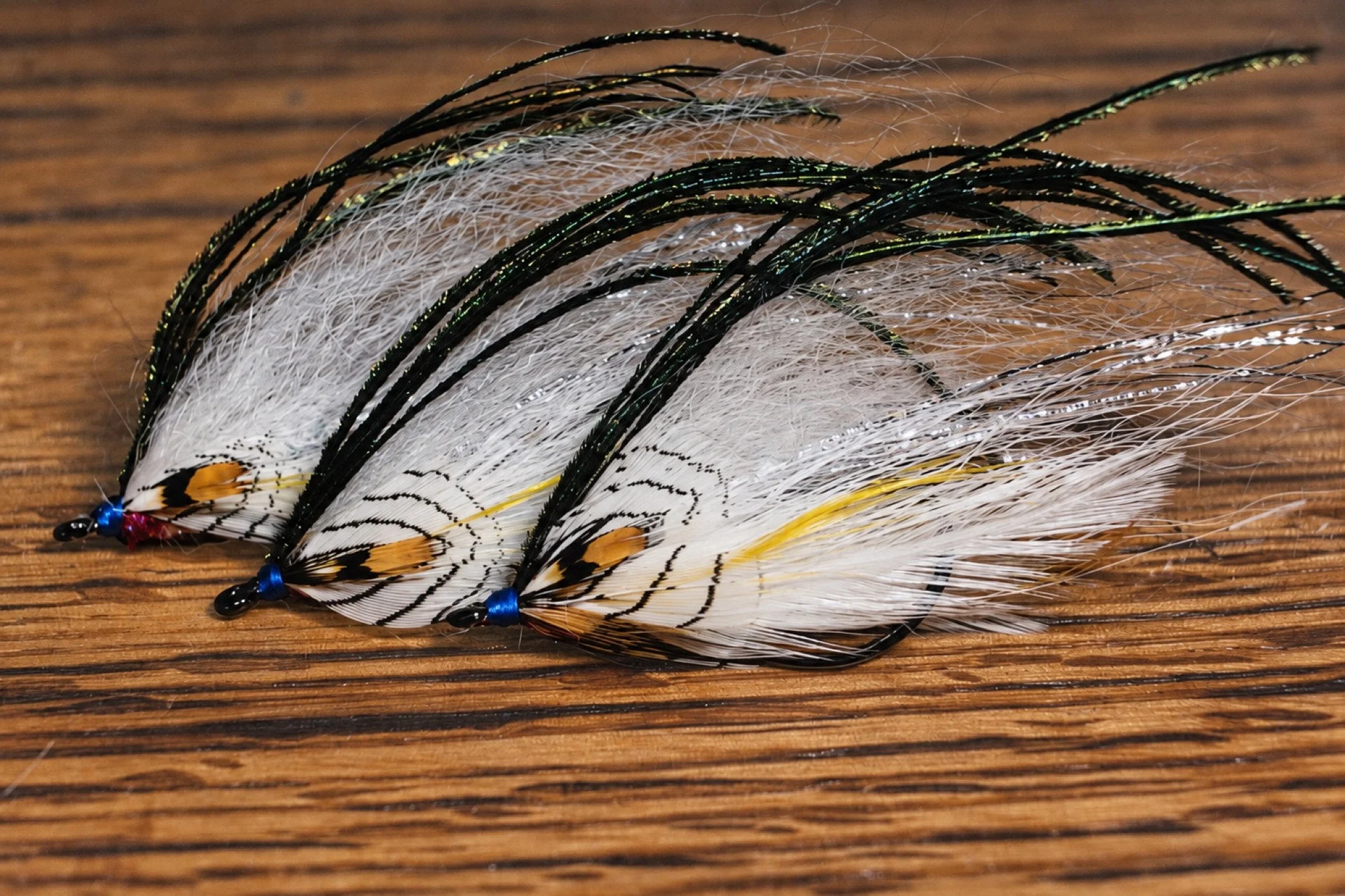 Three fully dressed Sheep Shad flies with white feathers and dark overwing, arranged on warm wood.