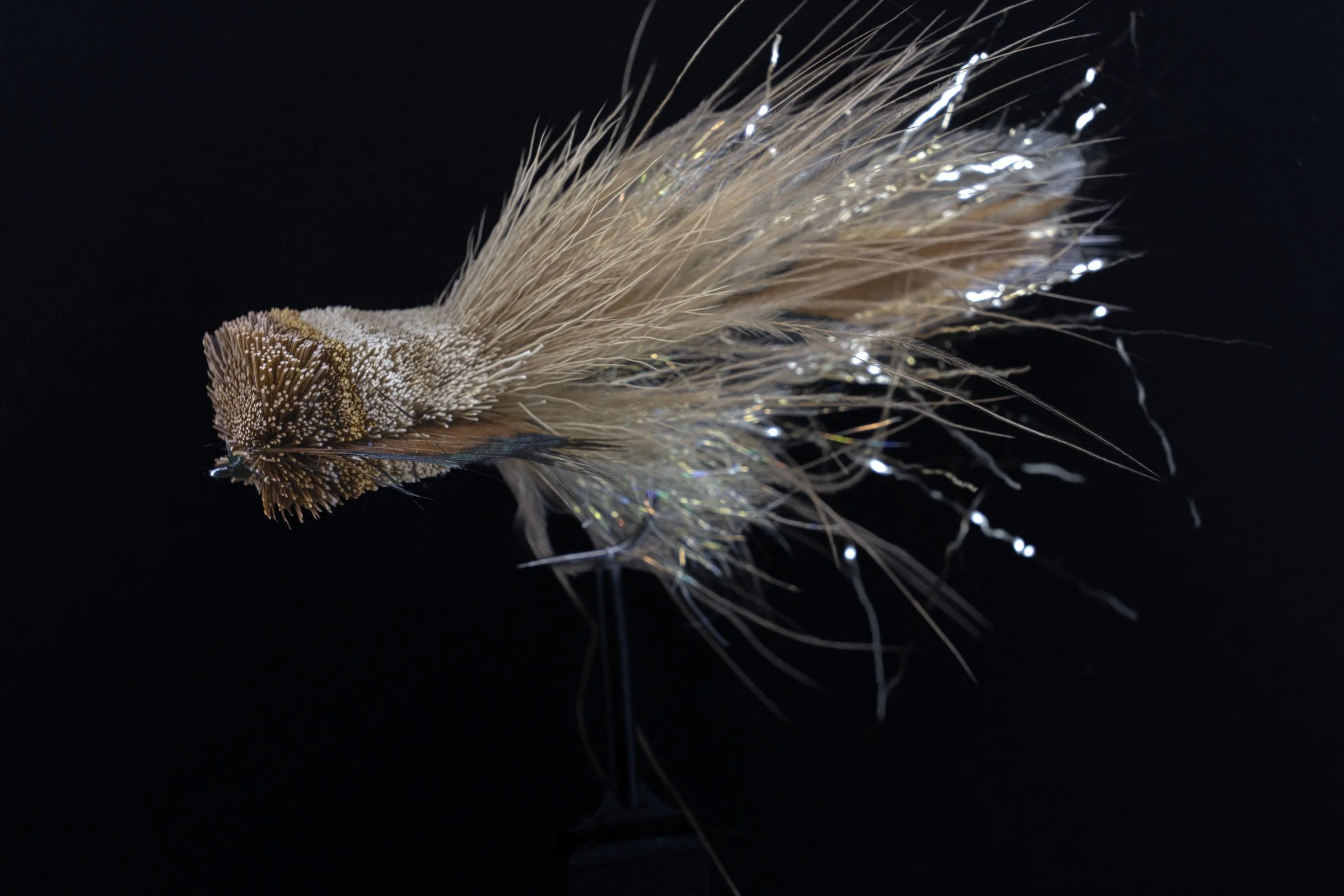 Finished pale deer-hair fly with a shaped head and reflective fibers against a dark background.