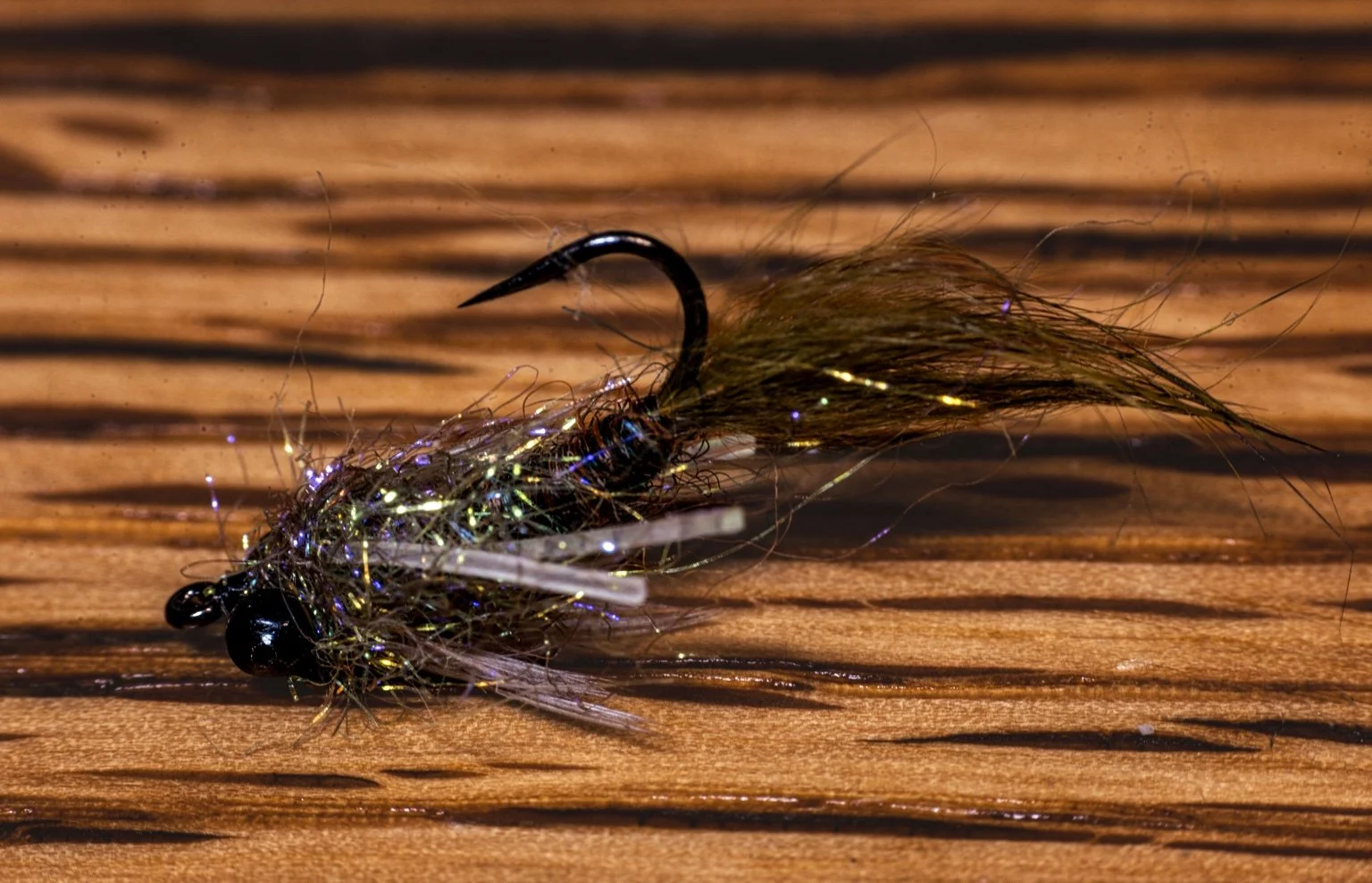 Finished olive Pan Handler fly with dark bead eyes on a wooden surface.