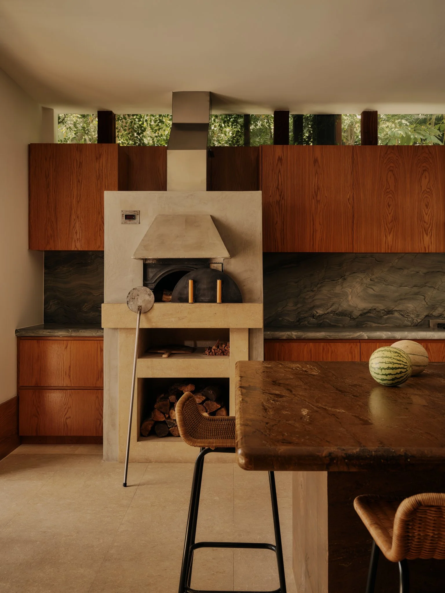 A cozy modern kitchen featuring a fireplace, wooden cabinets, a marble countertop, and two watermelons on a dark marble table.