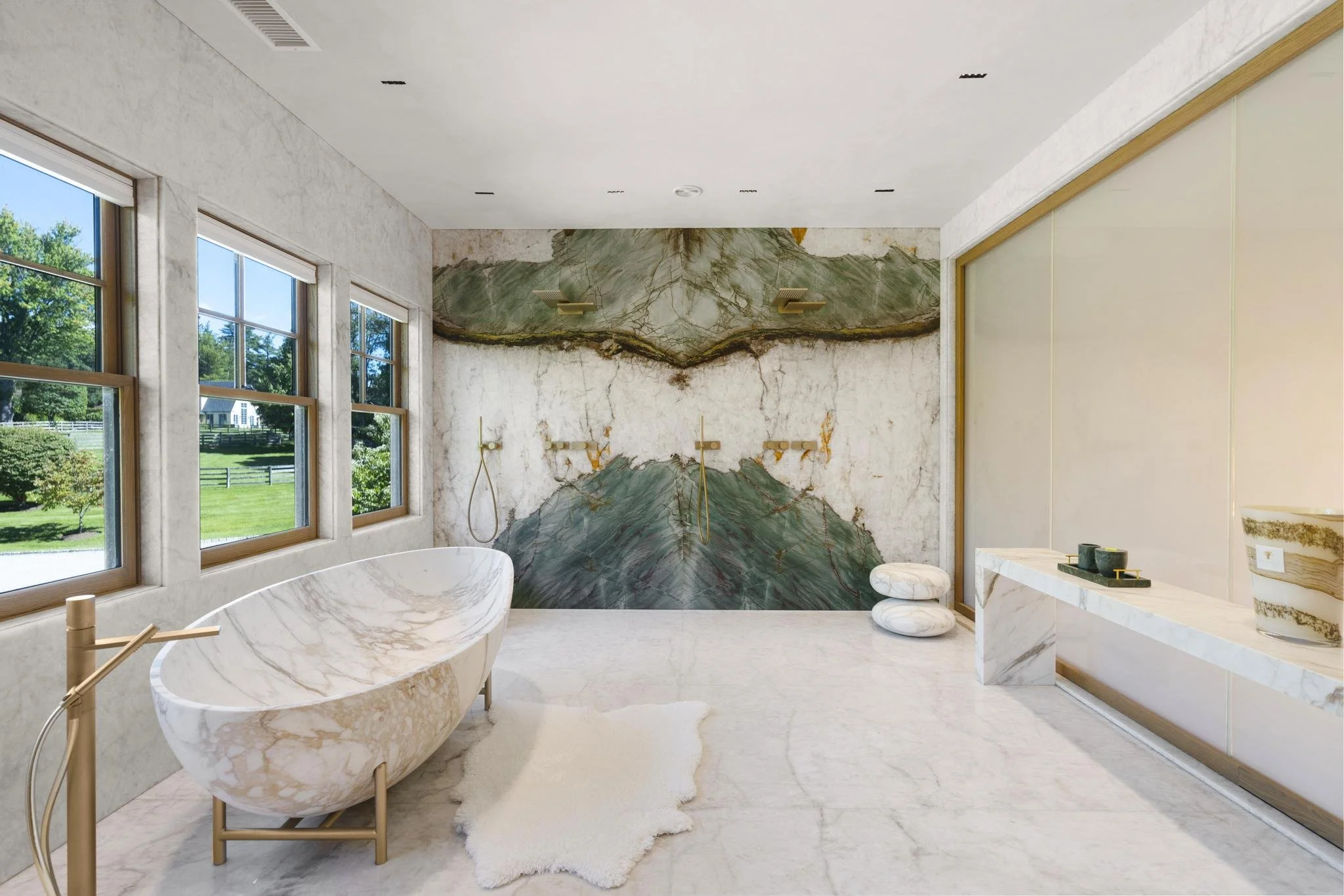 Luxurious bathroom with marble bathtub, marble walls, large windows showing a green outdoor landscape, and modern fixtures.