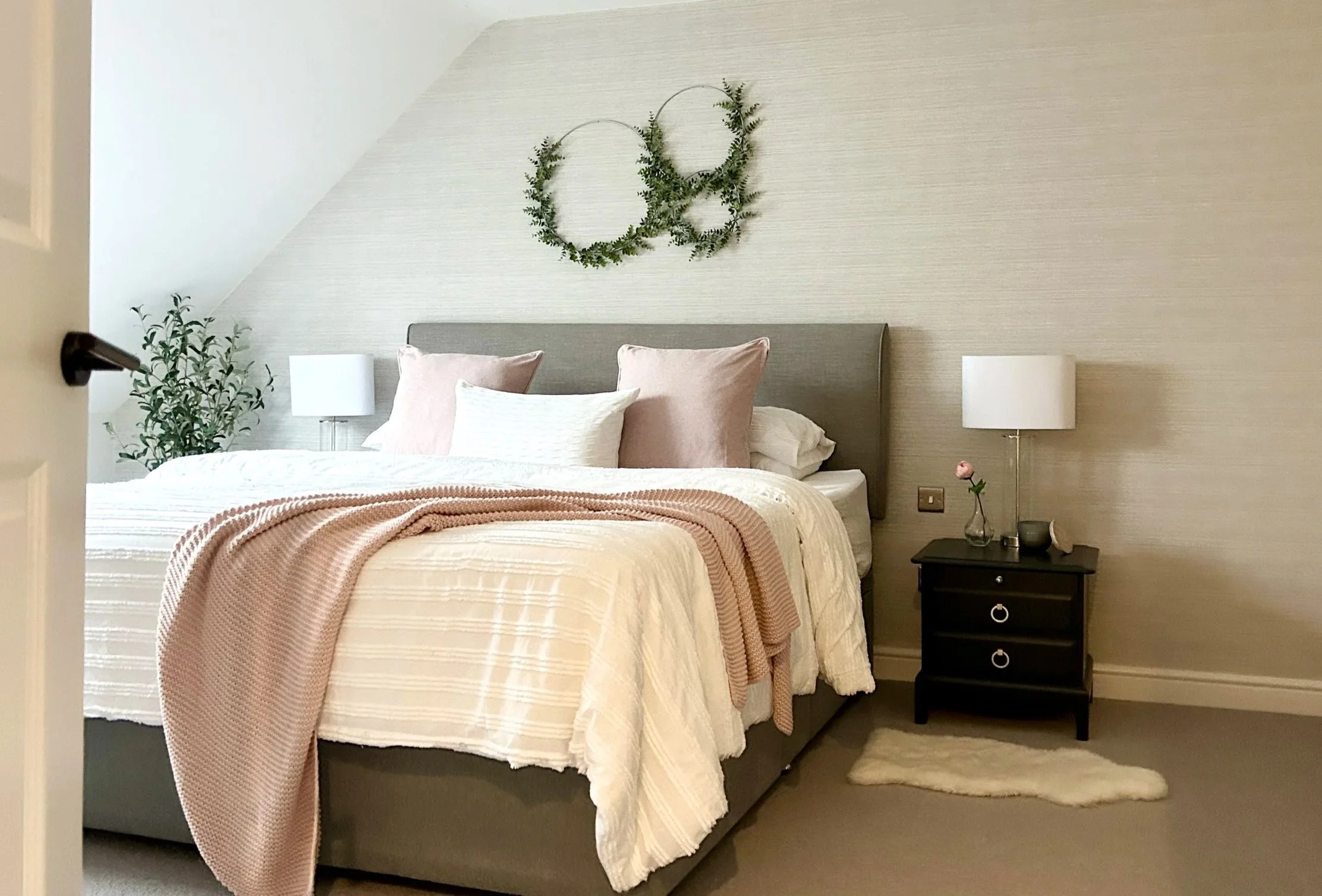 A bedroom with a bed, pillows, nightstand, and decorative greenery on the wall.