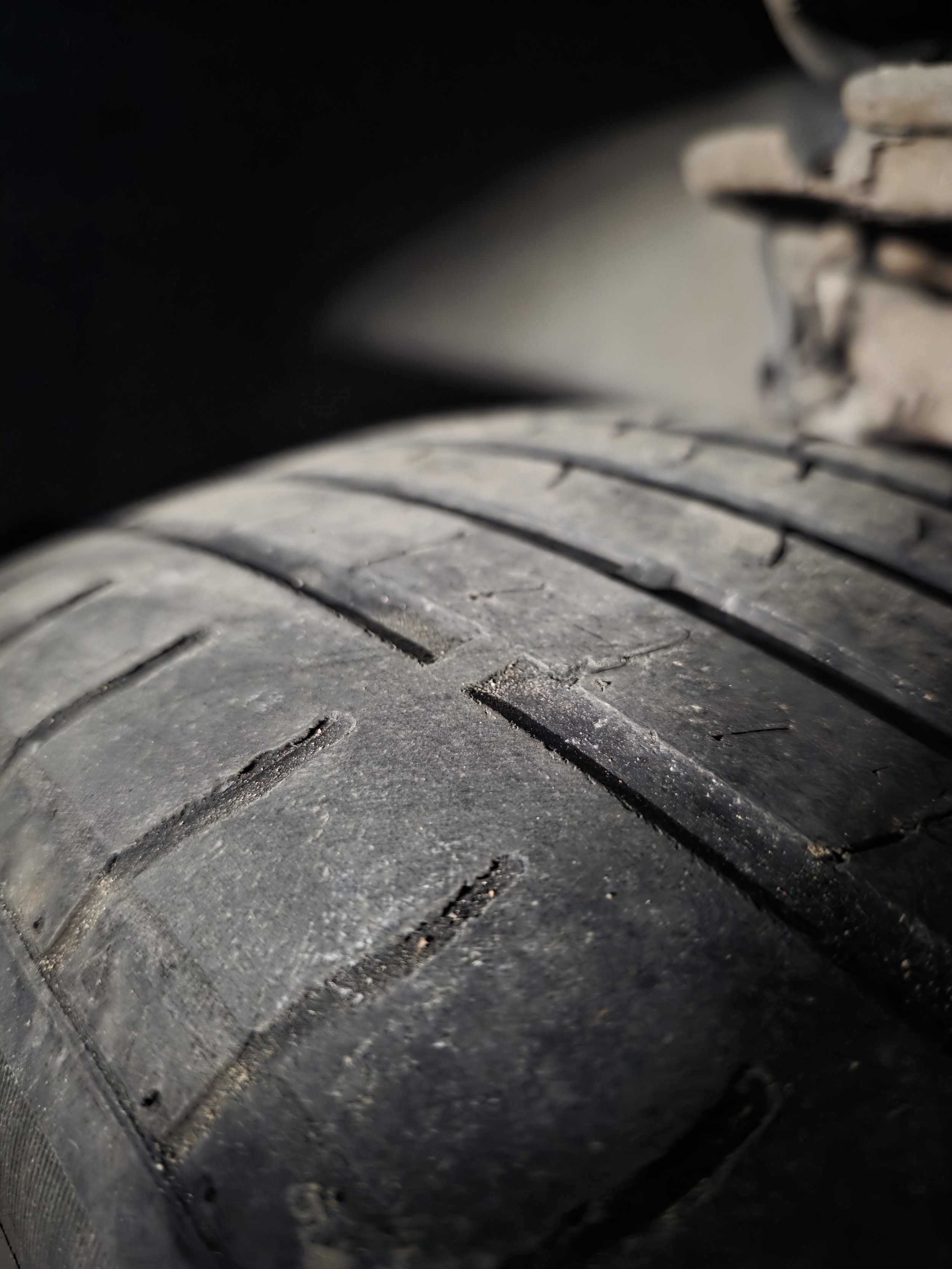 Close-up view of a worn black tire with visible treads, part of a vehicle, with some dirt and debris on the surface.
