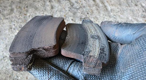 Close-up of a gloved hand holding a worn out and new brake component  pad with visible wear and cracking.