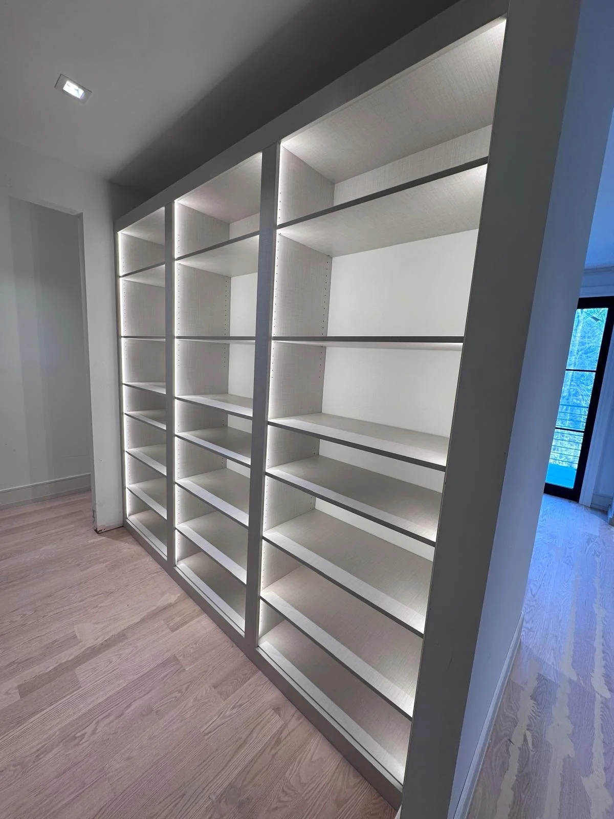 Modern walk-in closet with illuminated built-in white shelving and hardwood floors