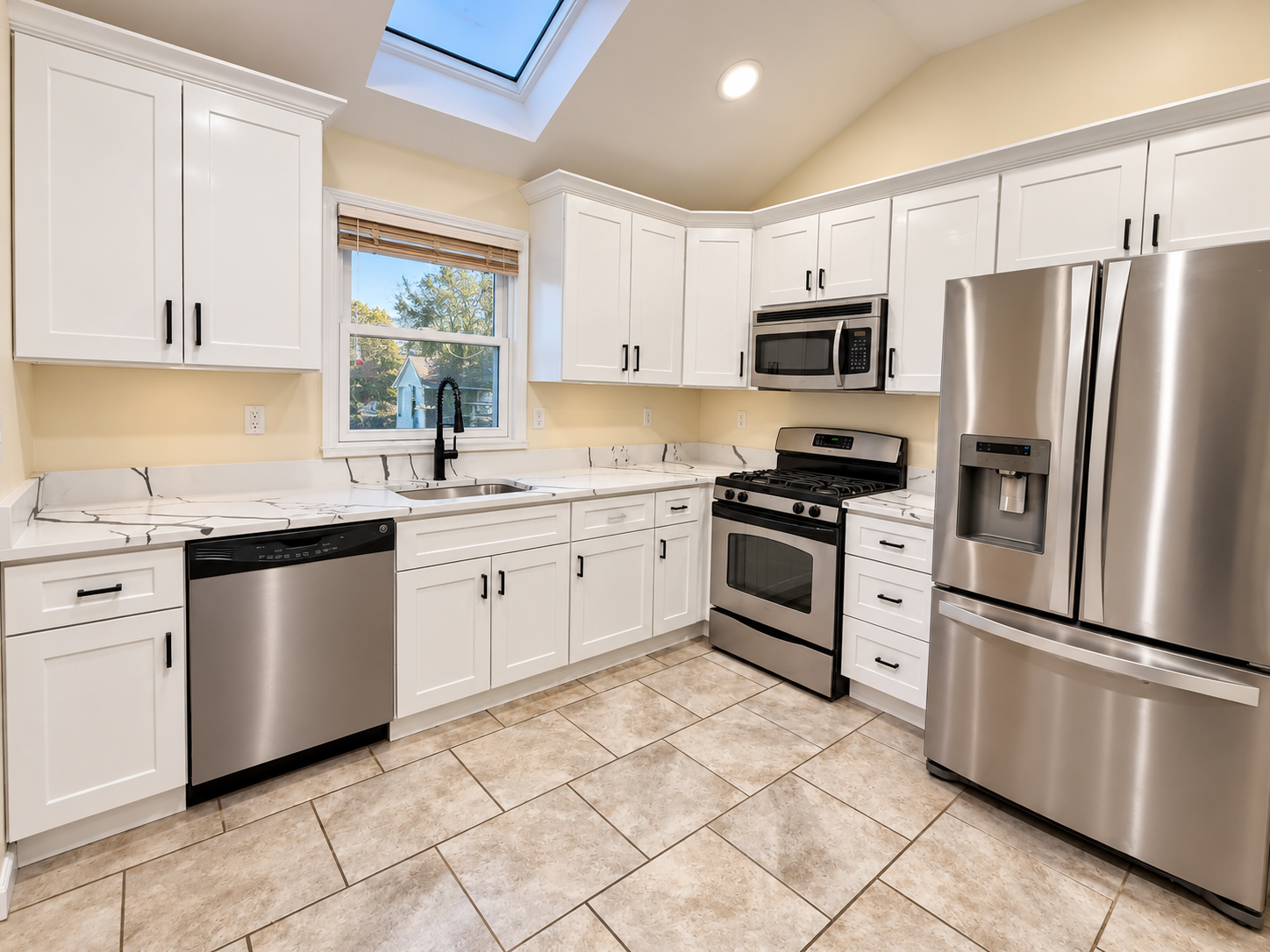 Bright remodeled kitchen with white cabinets, marble-look countertops, stainless steel appliances, skylight, and tiled floor
