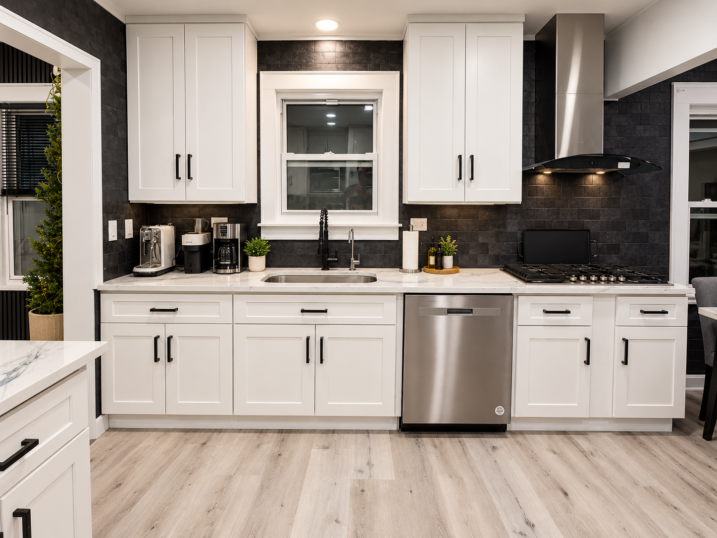 Modern white kitchen with black tile backsplash, marble countertops, stainless steel appliances, sink, gas range, and coffee station