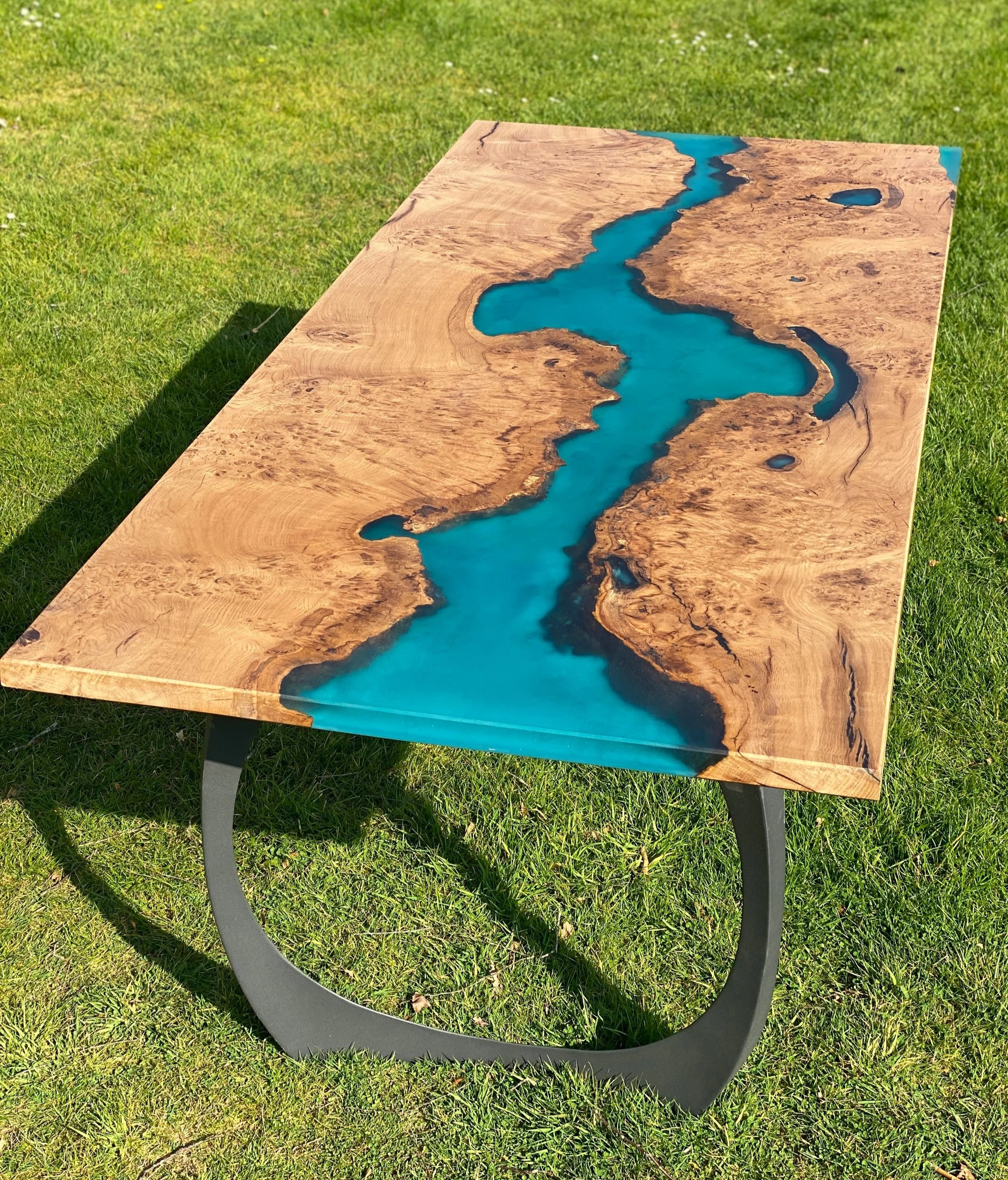 Turquoise epoxy resin river table with steel legs in a sunny garden