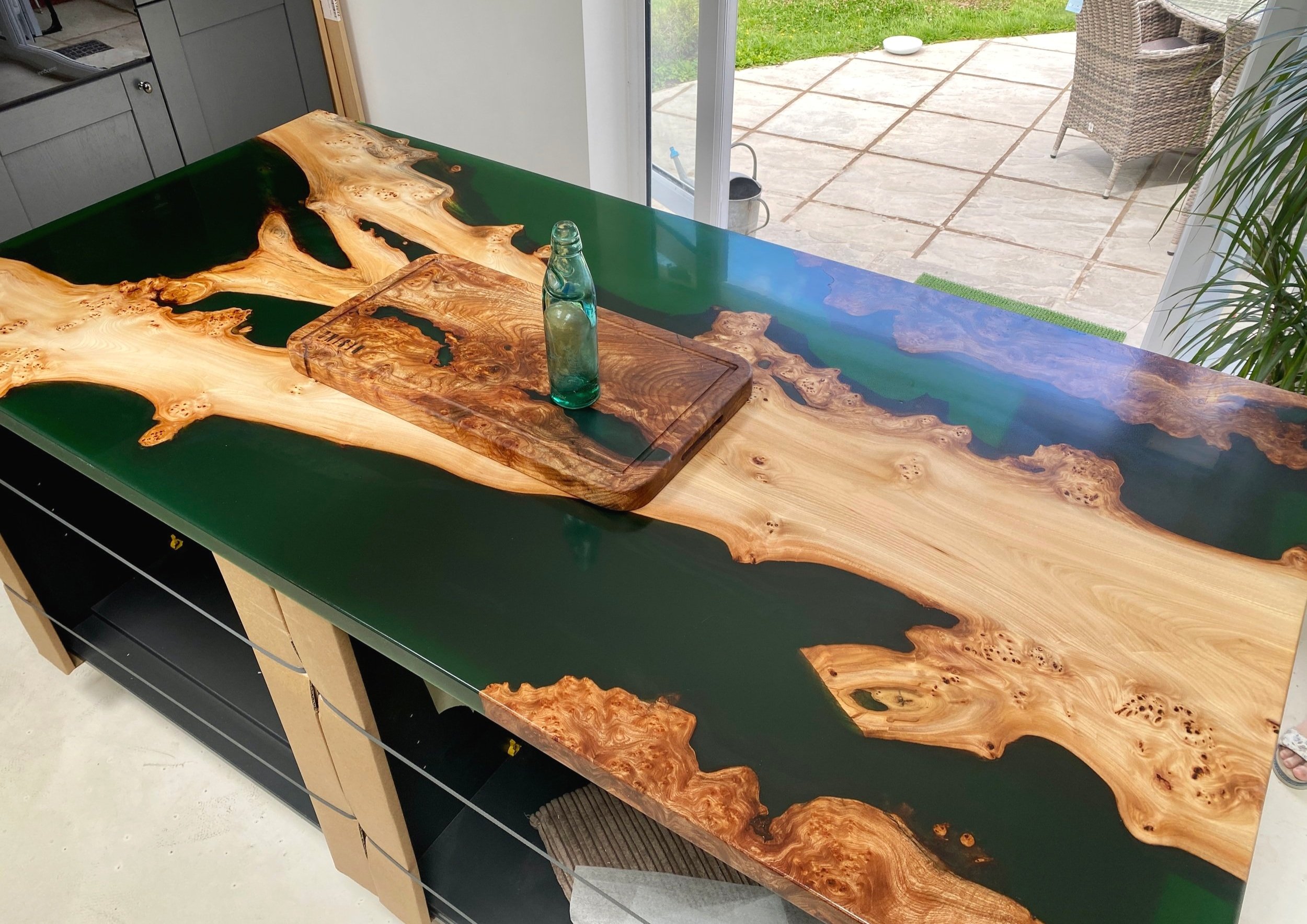Deep green epoxy resin kitchen island with crotch piece of elm running though and matching chopping board