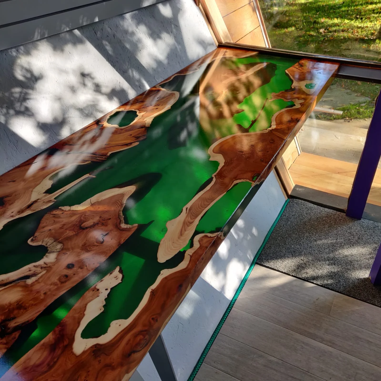 End view of an emerald green and english yew epoxy resin desk sat in a garden office dappled in sunlight