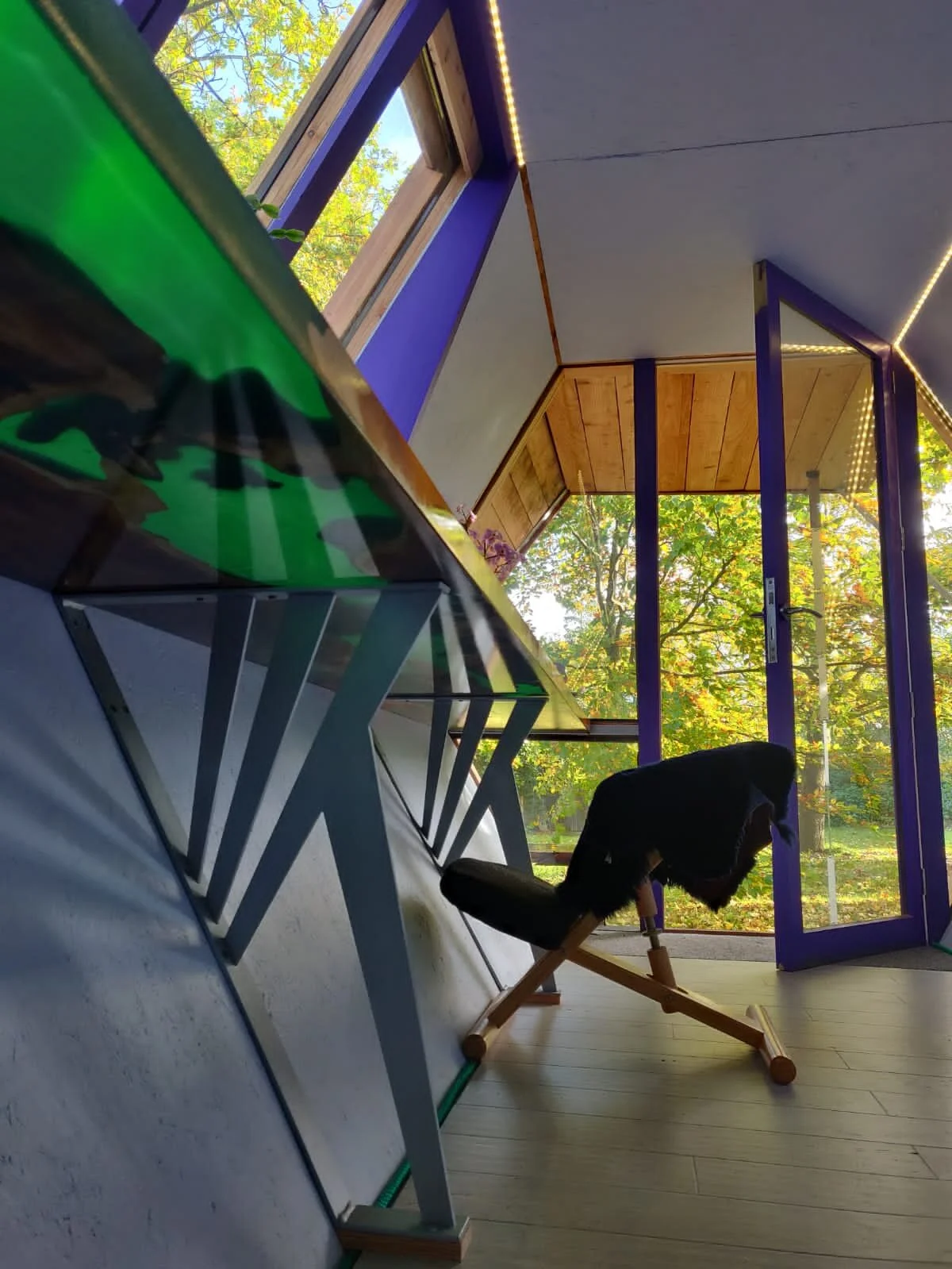 underside of an epoxy resin and wood garden office desk showing translucent resin and steel support legs with ergonomic desk chair and open door