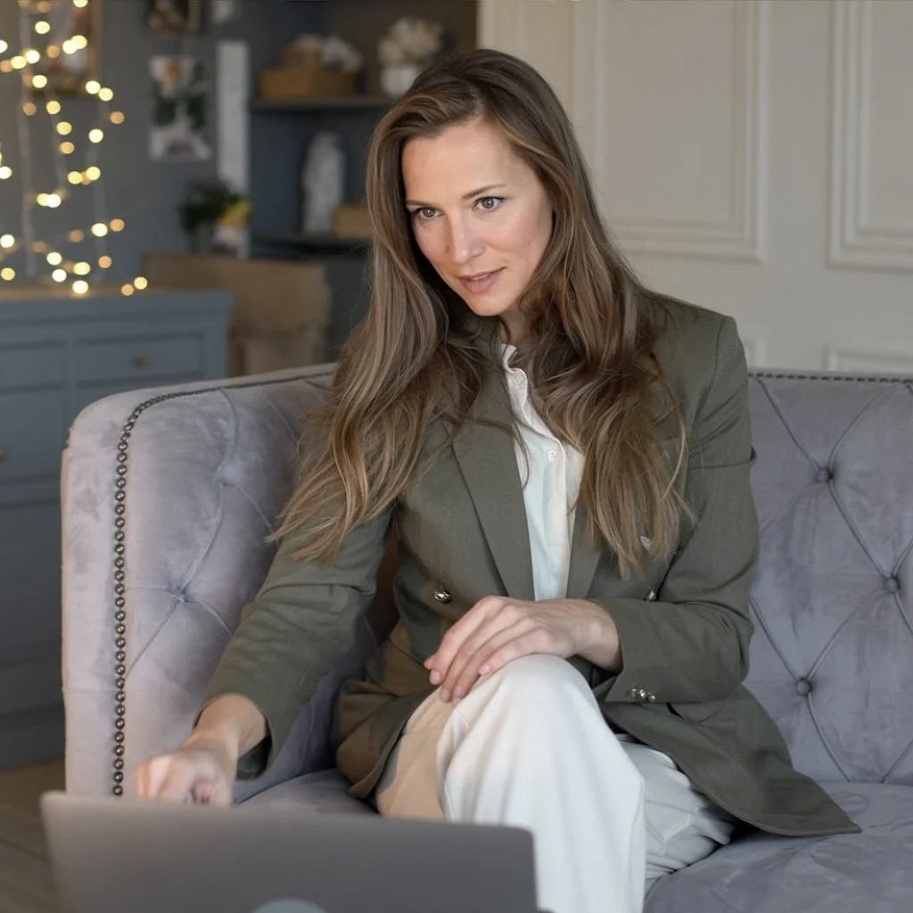 Professional woman in an olive blazer using a laptop while seated on a tufted gray sofa