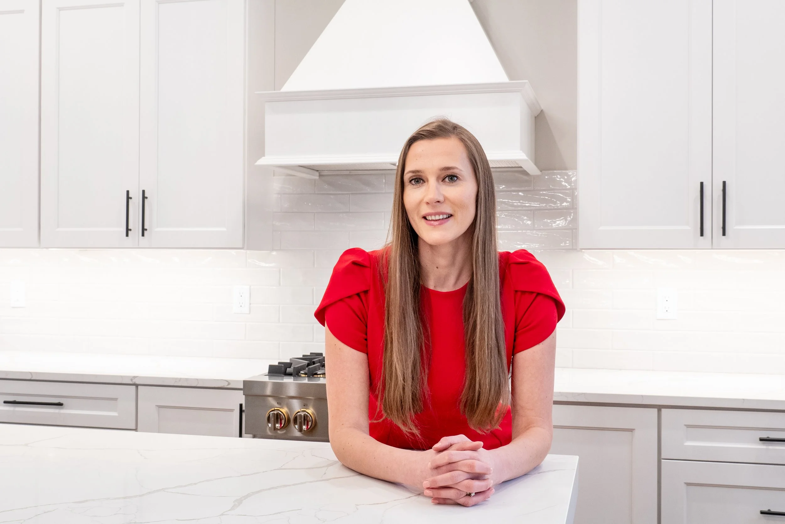 Woman in a red blouse standing behind a white kitchen island in a bright modern kitchen