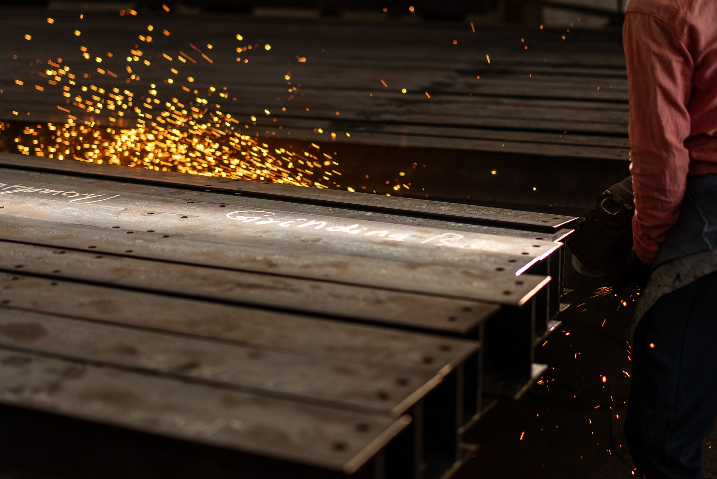 Worker grinding metal sheets on an industrial cutting table, sending bright orange sparks across the workshop.
