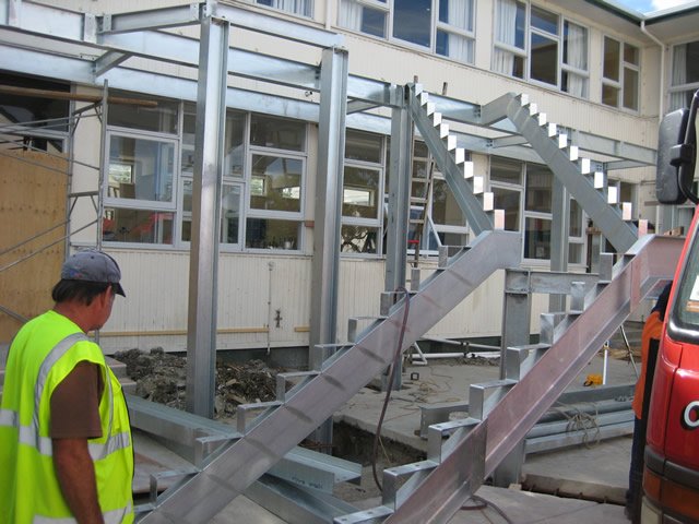 Construction worker in a high-visibility vest inspecting unfinished metal stairs and framing outside a building