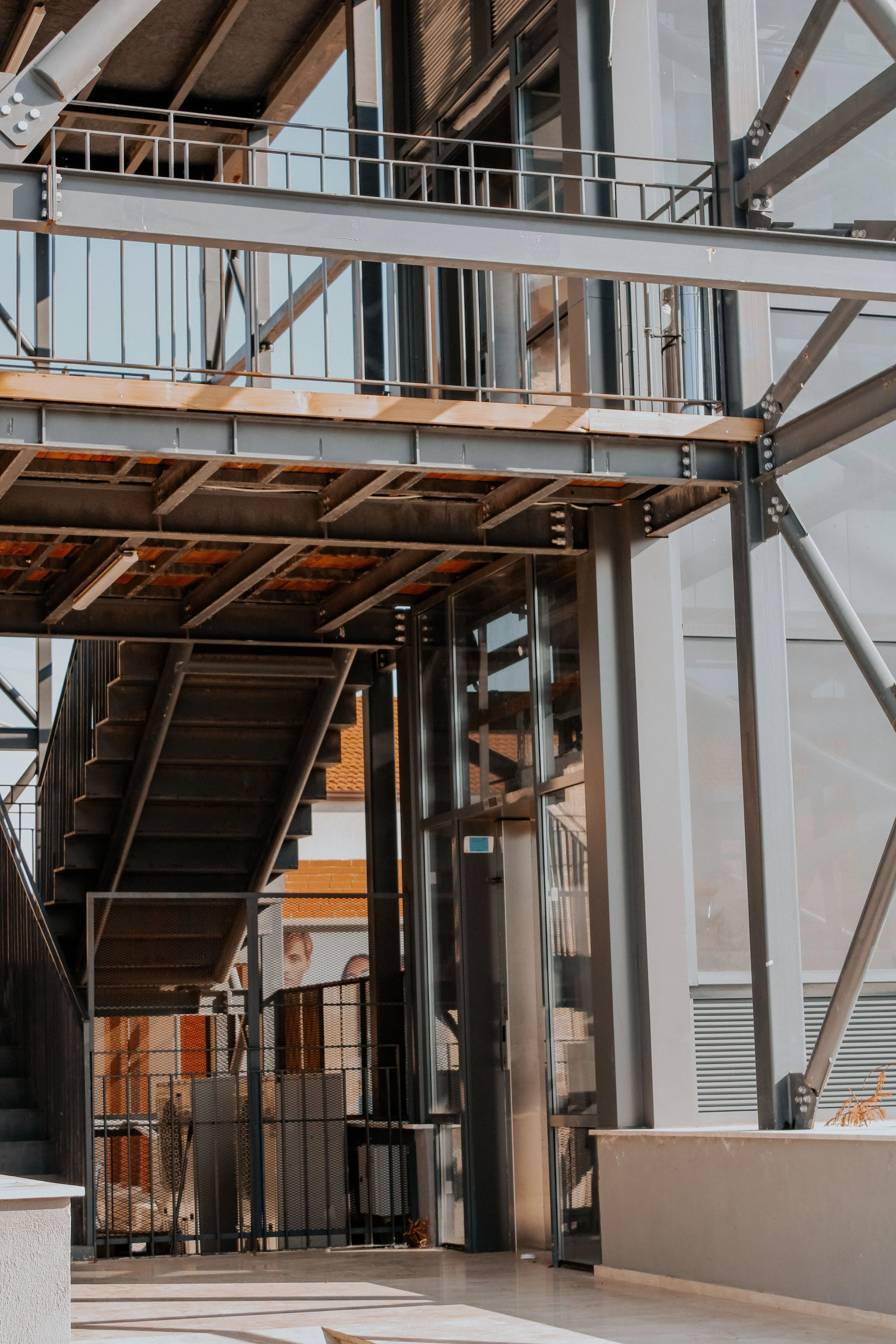 Modern building exterior with exposed steel beams, metal staircases, railings, and large glass windows