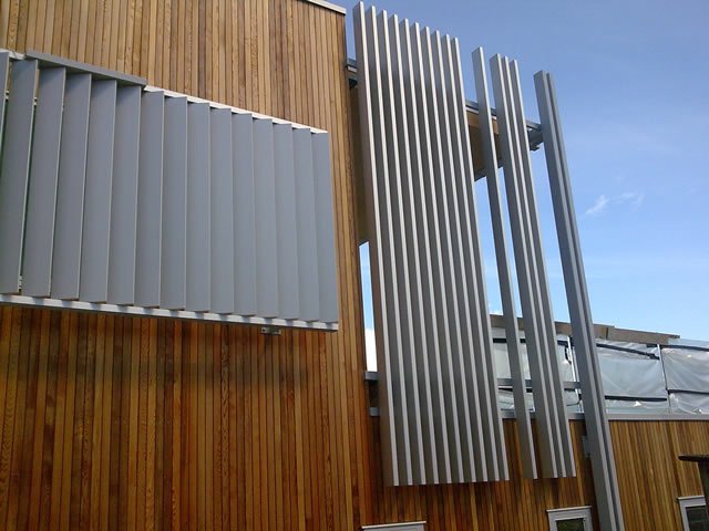 Modern building facade with vertical wood siding and gray metal architectural fins against a blue sky