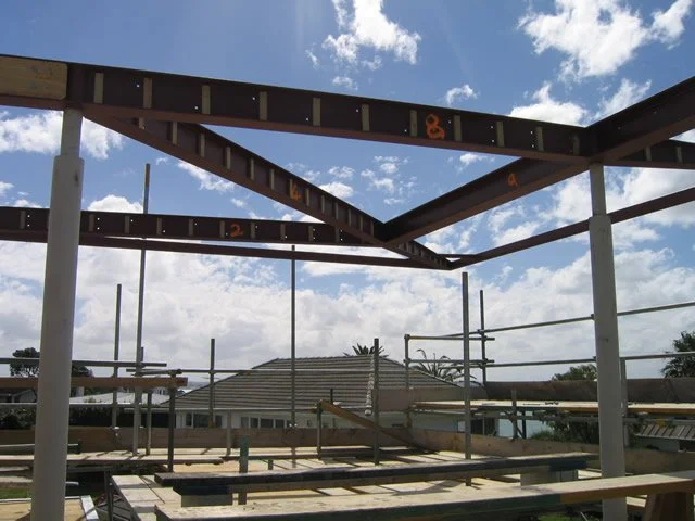 Steel building framework under construction against a blue sky with clouds