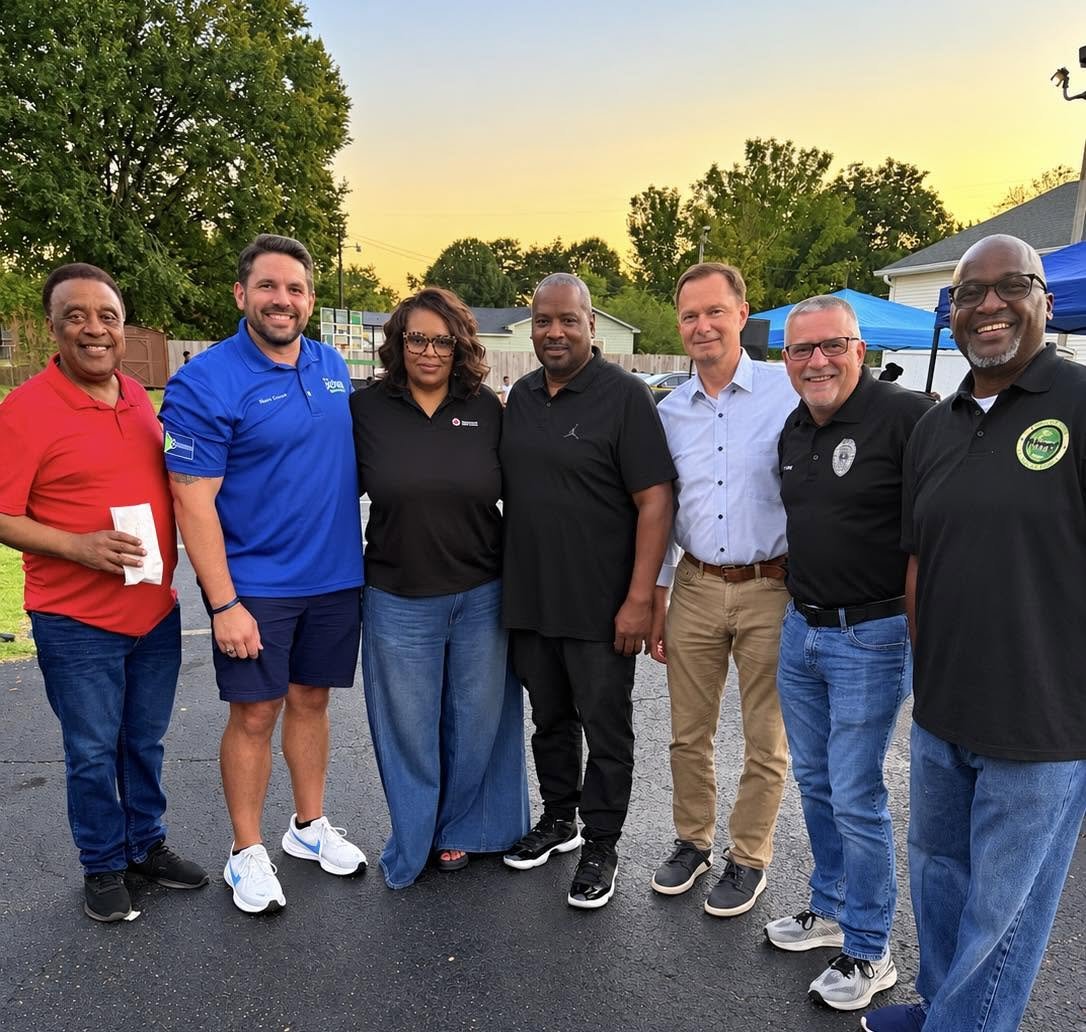 Scott Conger with a group of adults smiling and standing side by side outside during sunset, with trees and a house in the background.