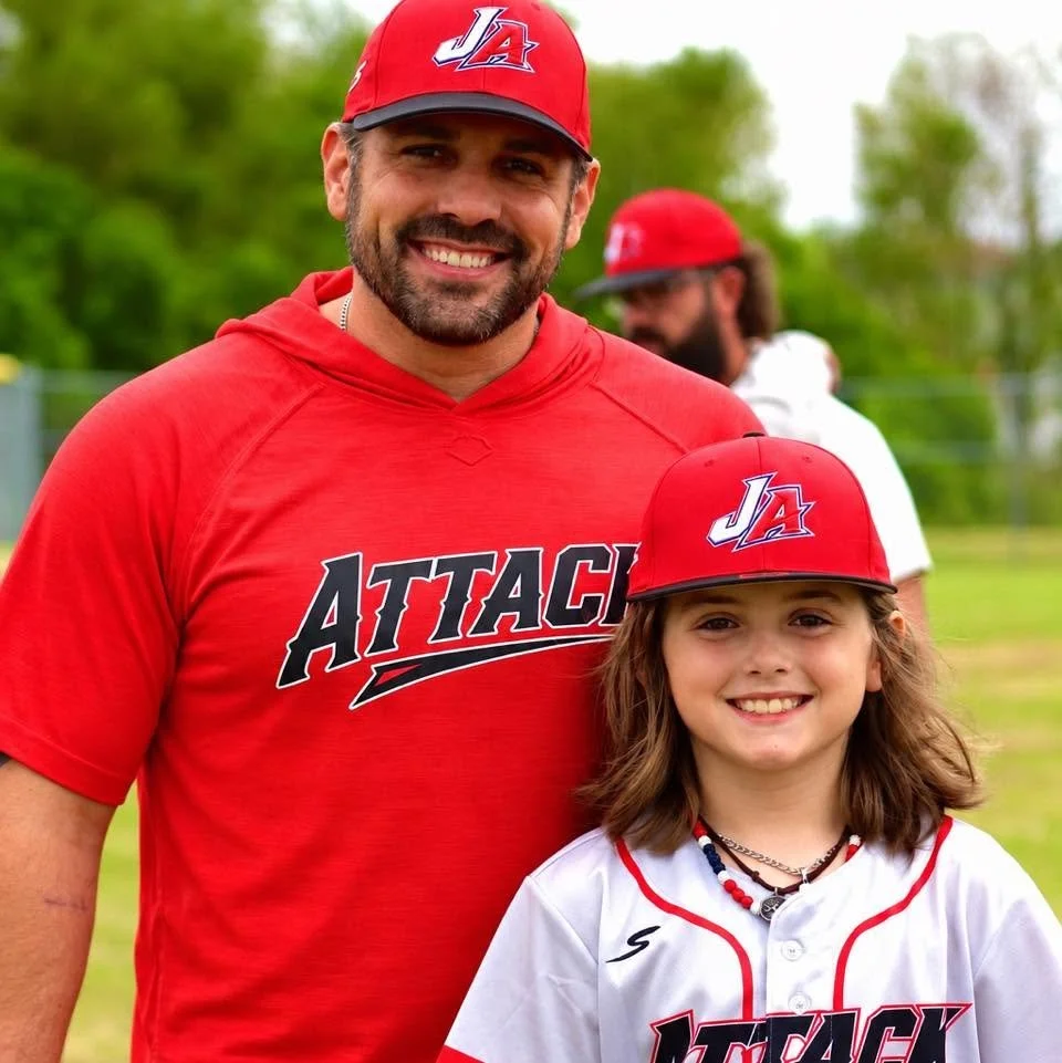 Mayor Scott Conger and his son smiling at the camera wearing baseball team gear