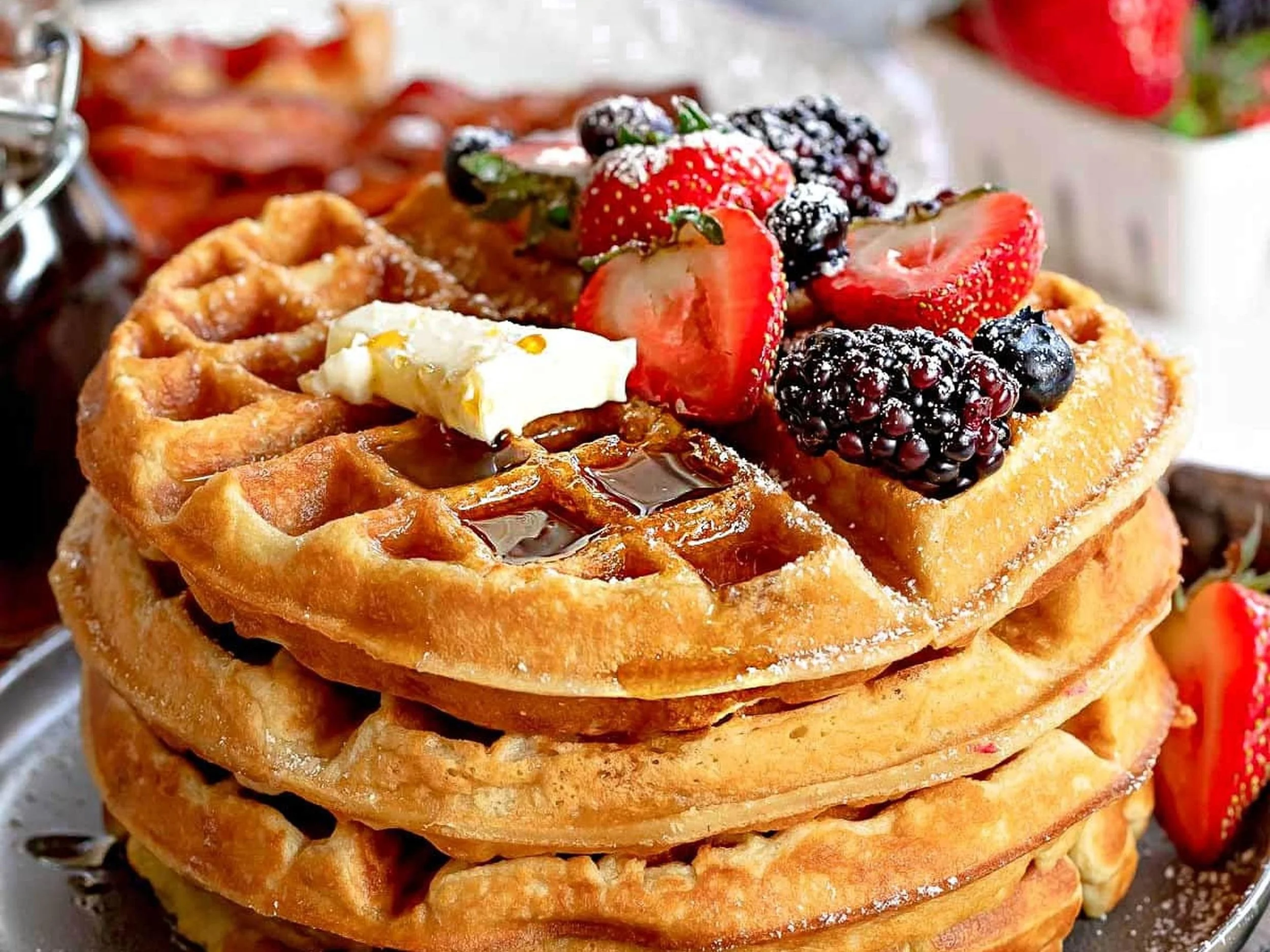 Stack of waffles topped with a variety of fresh berries, a piece of butter, and syrup.