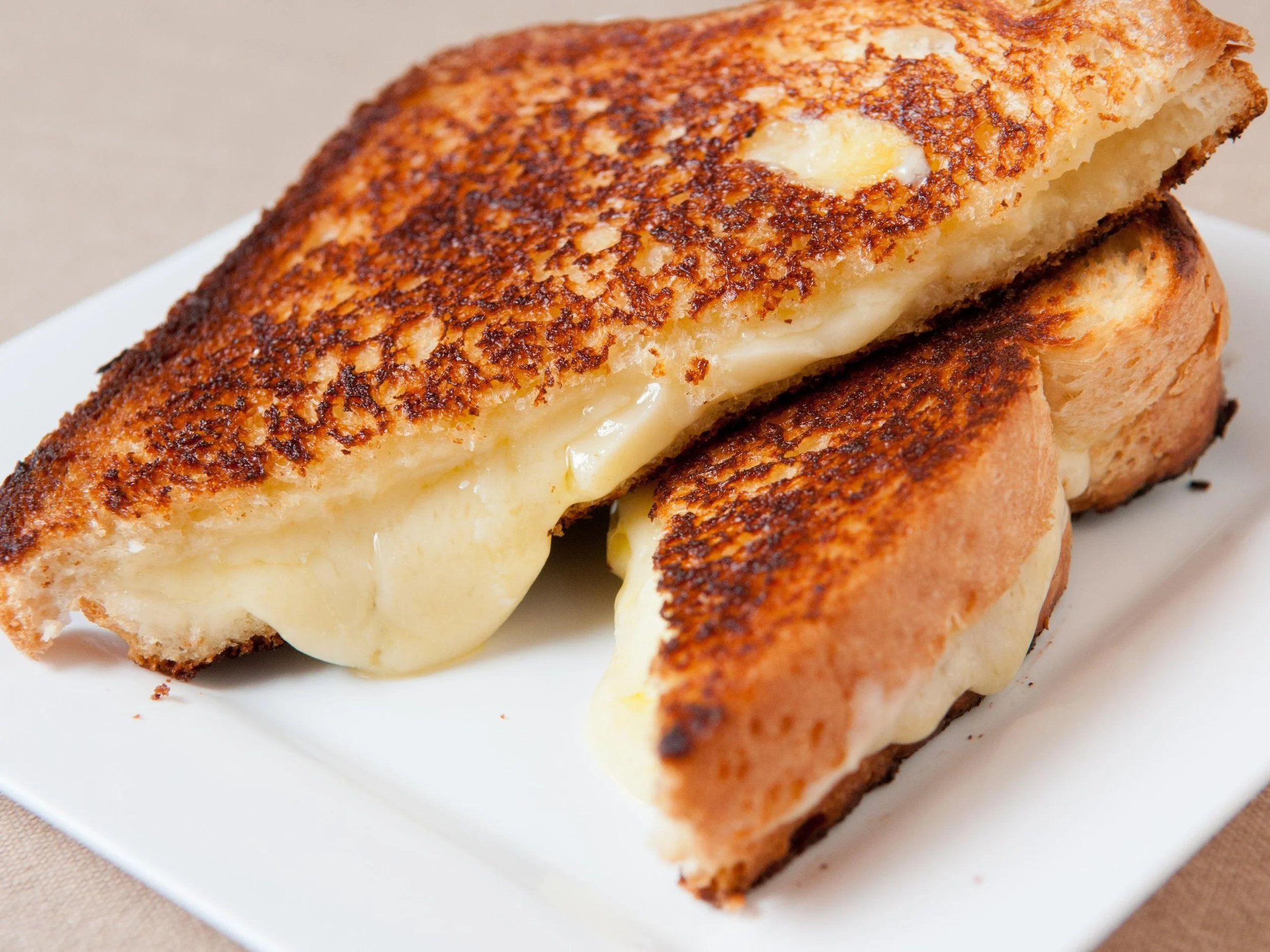 A close-up of a grilled cheese sandwich with melted cheese oozing out, on a white plate.