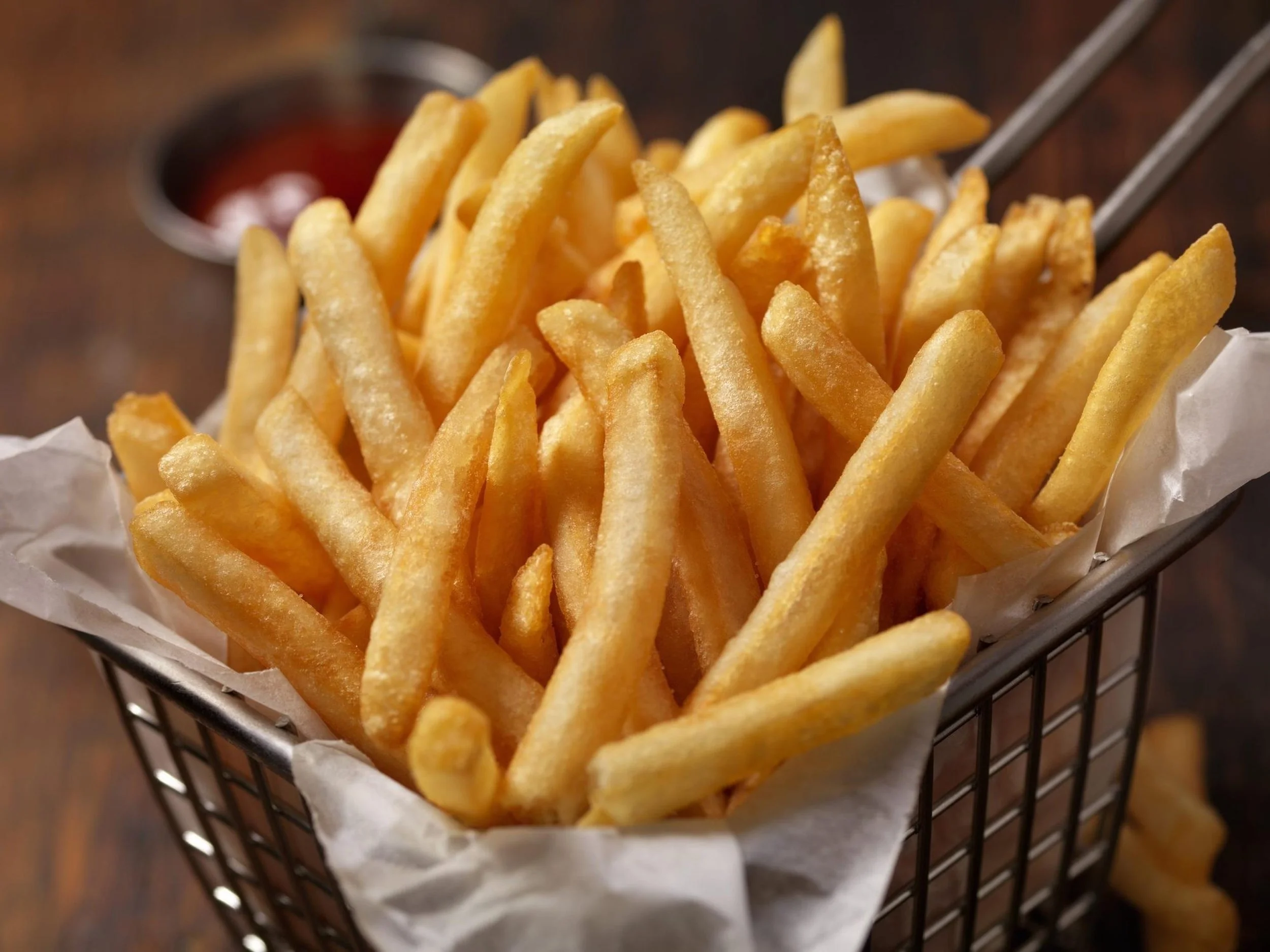 Close-up view of a basket of French fries with ketchup in the background.