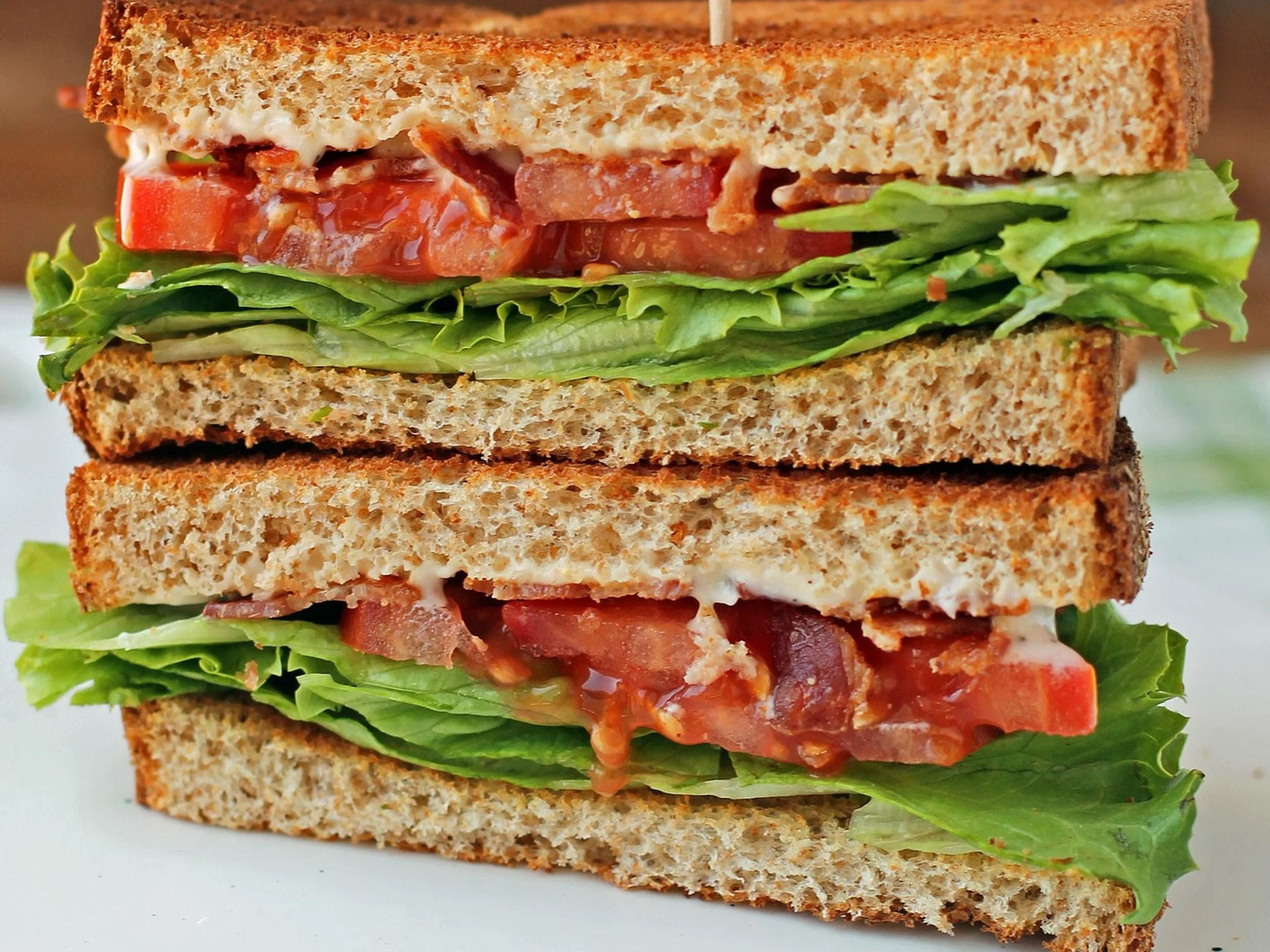 A close-up of a multi-layered sandwich with lettuce, tomato, bacon, and mayonnaise between slices of toasted bread.