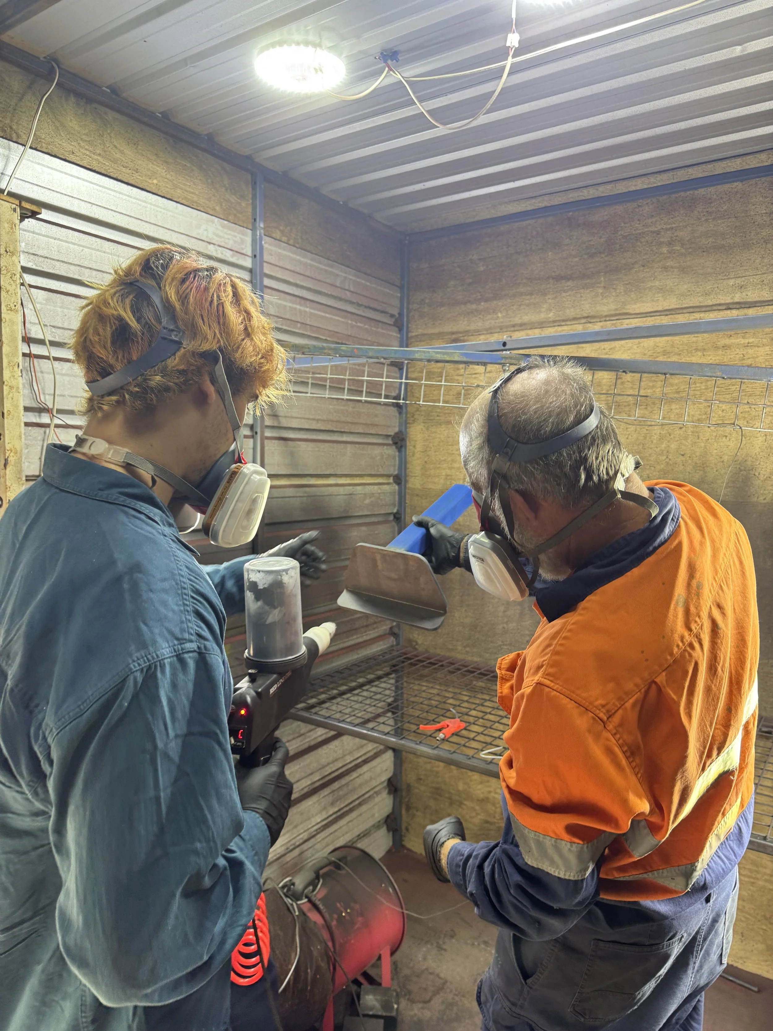 Two workers in protective gear and headphones working on a project in a workshop, with tools and equipment around them.