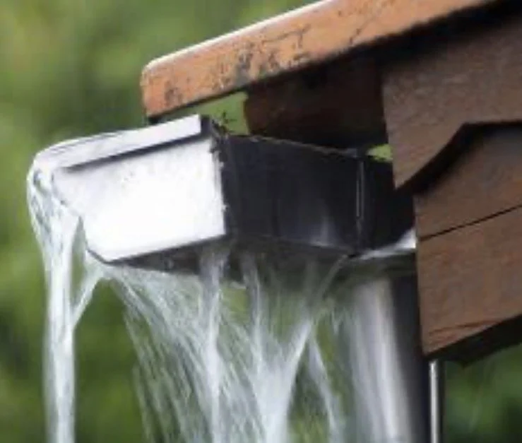 Water overflowing from a black and white gutter attached to a wooden roof edge.