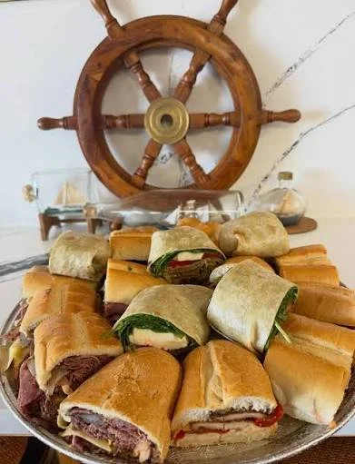 A tray of assorted sandwiches and wraps with a ship's wheel decor in the background.