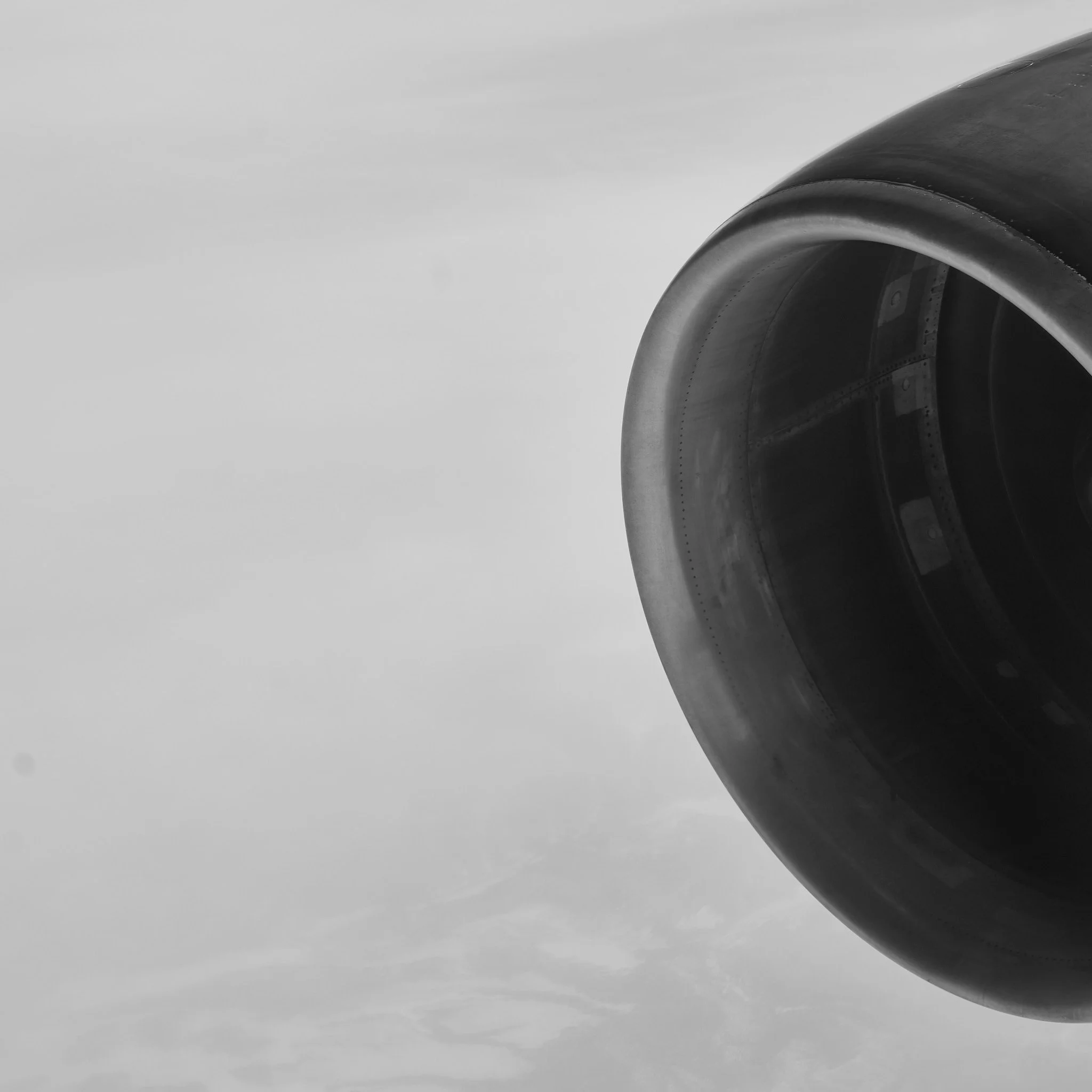 Close-up of an aircraft jet engine against cloudy sky, black and white photo.