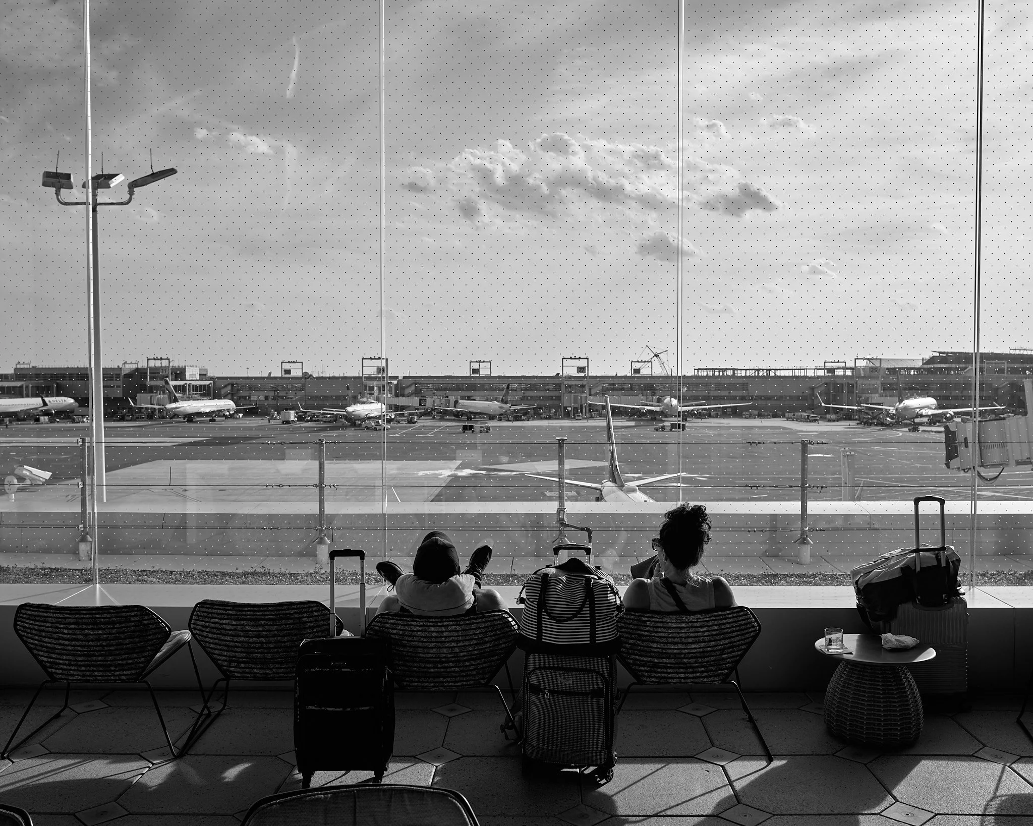 People sitting in an airport lounge watching planes on the tarmac through a large window 