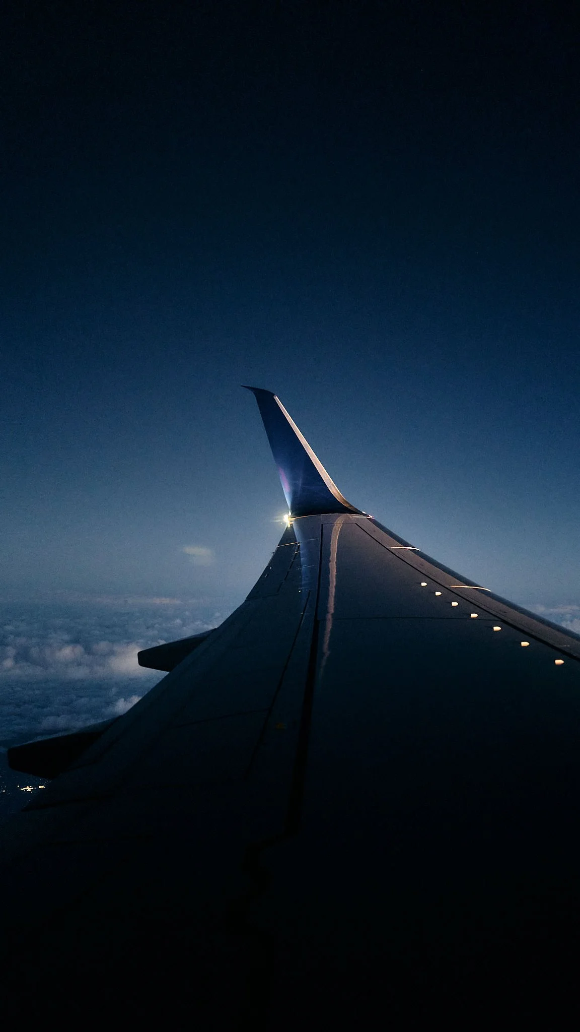 View of an airplane wing at night, with a dark sky and clouds below. photo by Matt Ellis