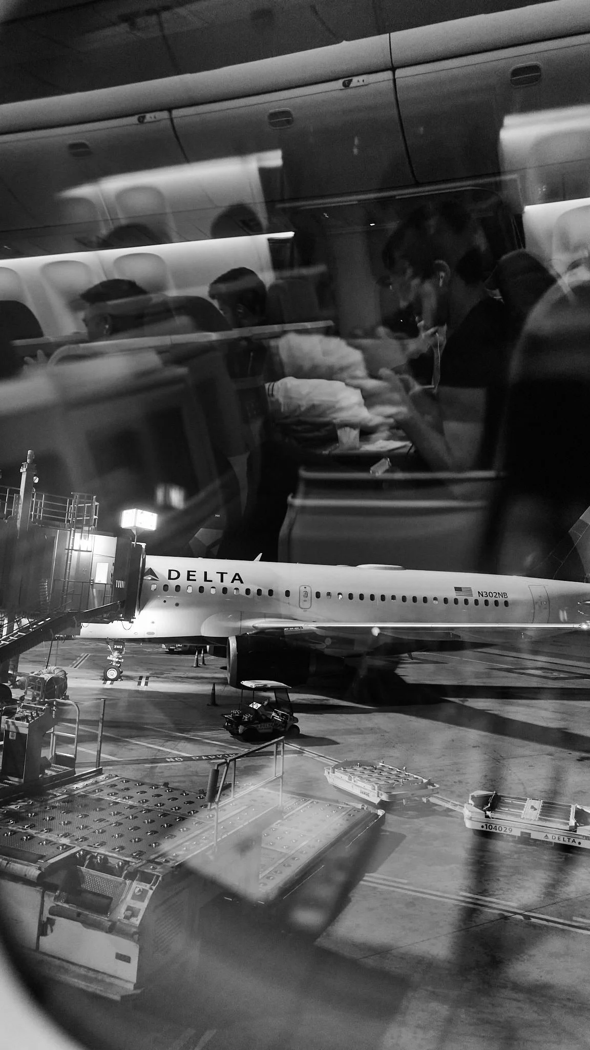 People sitting inside an airplane, applied with reflections from the airport window, with an airplane and airport ground vehicles outside.