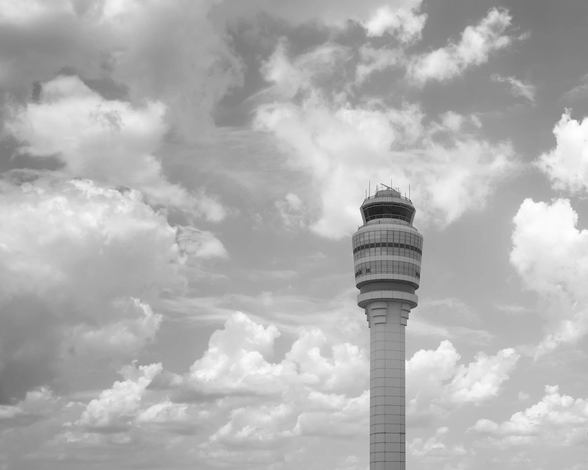 Black and white photo of an airport control tower with a cloudy sky in the background  by Matt Ellis