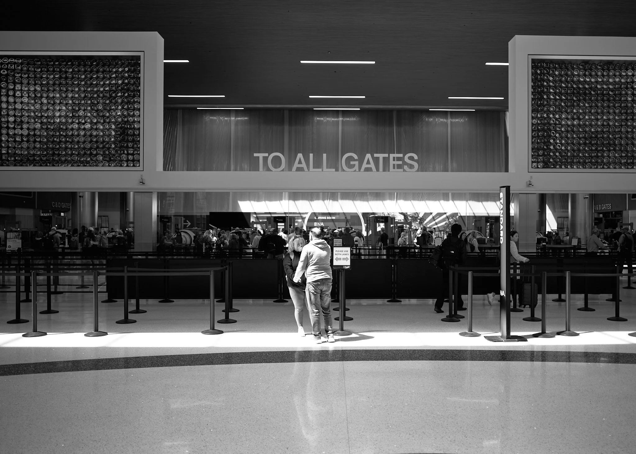 People waiting in line at an airport check-in counter with a sign indicating to all gates  by Matt Ellis