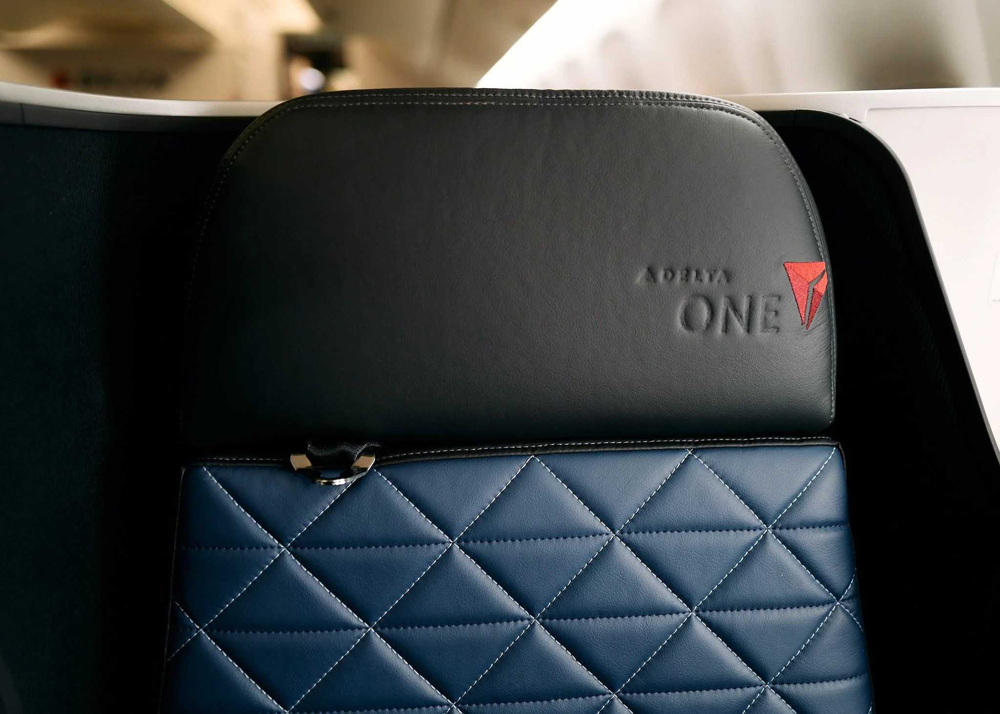 Black leather Delta One amenity kit and blue quilted leather pillow case on a tray table inside an airplane cabin.